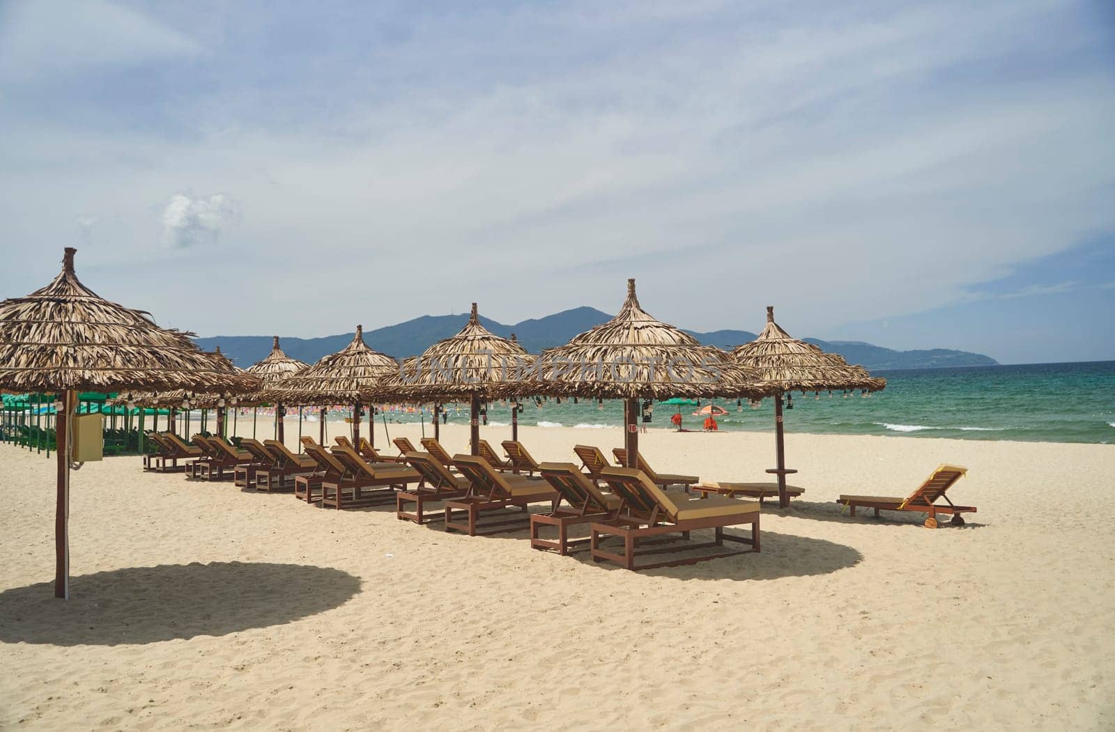 Straw sunshades and sunbeds on the empty pebble beach with sea in the background. Deserted beach with rattan sun loungers and umbrellas