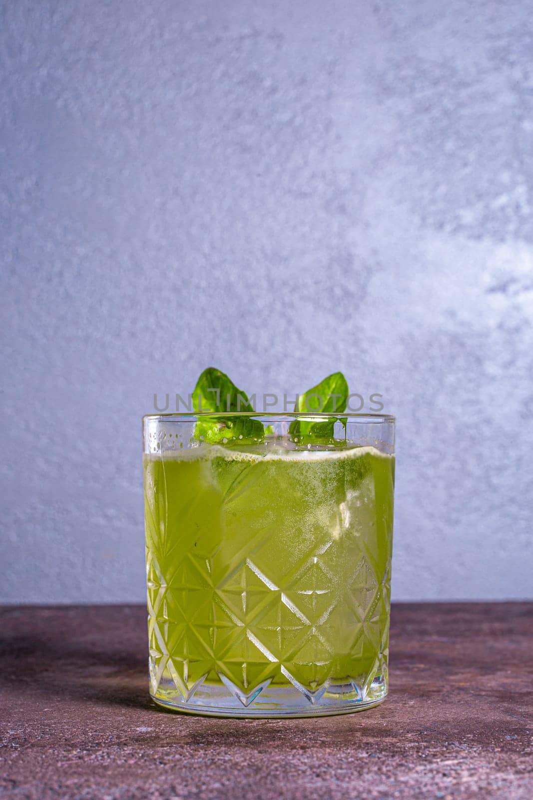 green cocktail in a glass with ice and a mint leaf.