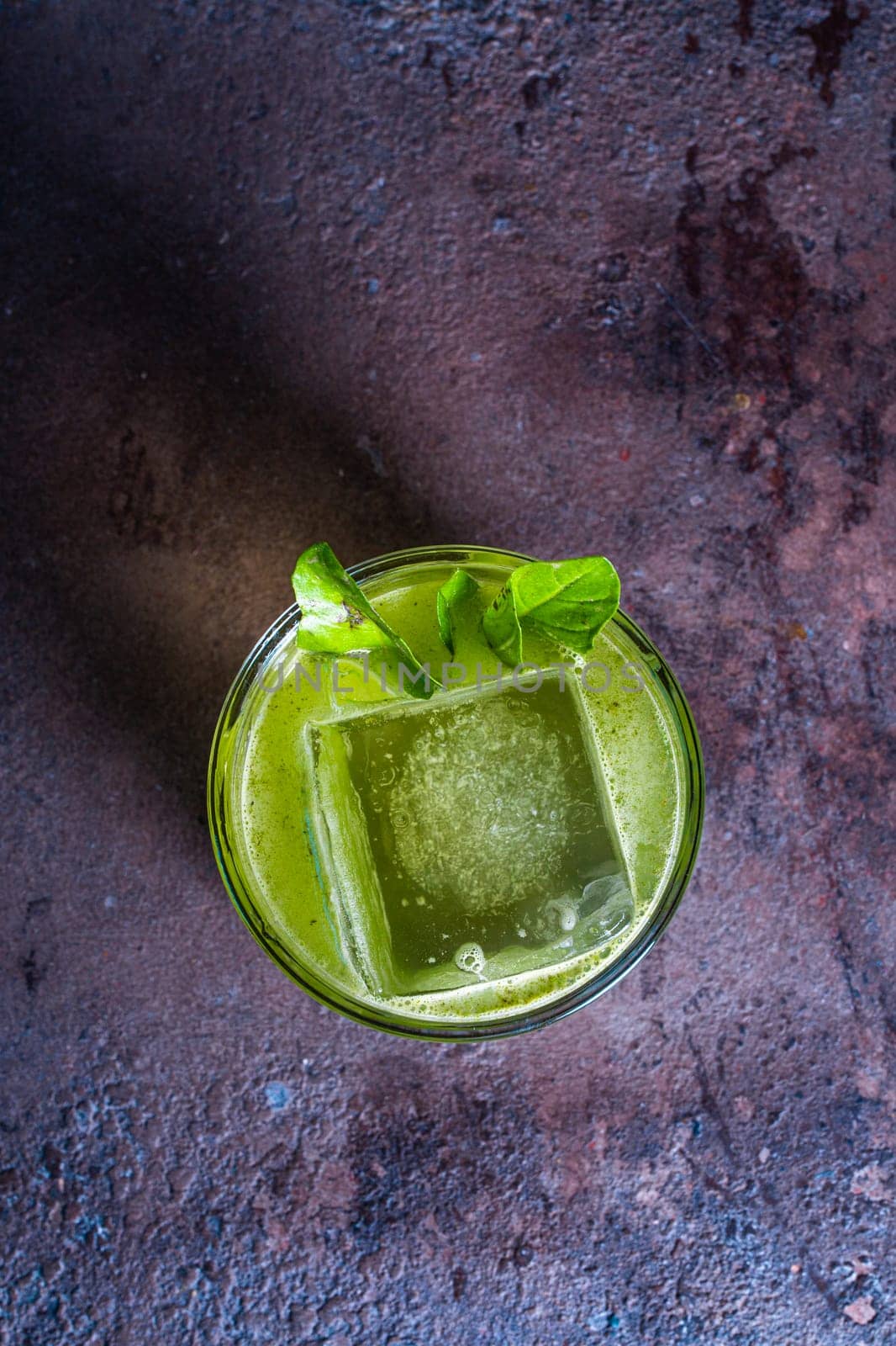 top view of a green cocktail in a glass with ice and a mint leaf on a textured background by Pukhovskiy
