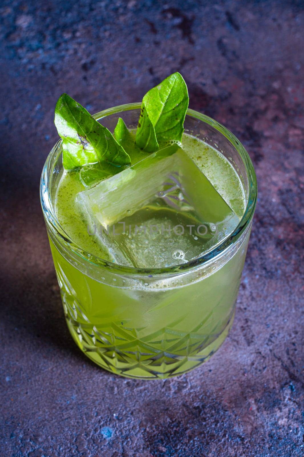 top view of a green cocktail in a glass with ice and a mint leaf on a textured background by Pukhovskiy