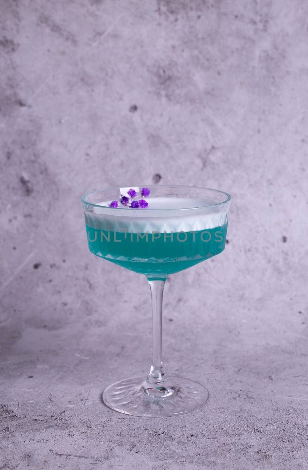 turquoise cocktail with a flower on a gray background.