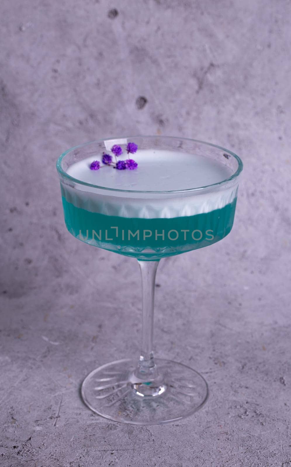 turquoise cocktail with a flower on a gray background.