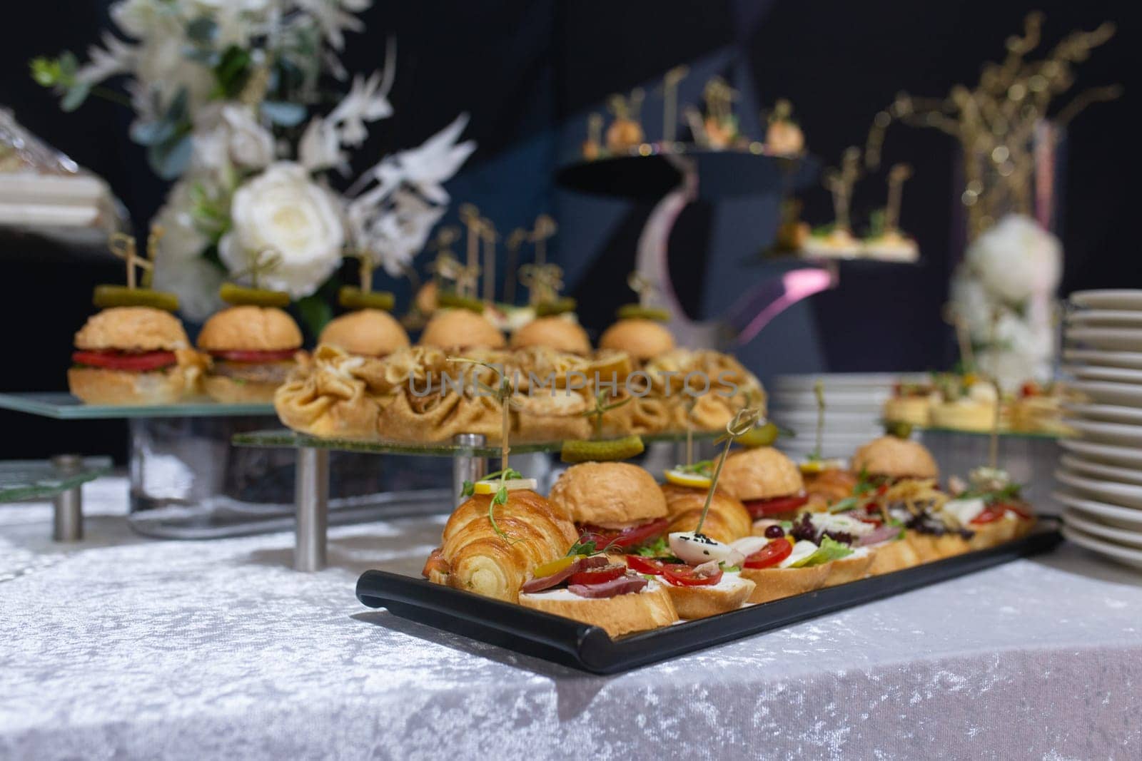 Croissants, burgers and various snacks on stands on the buffet table.