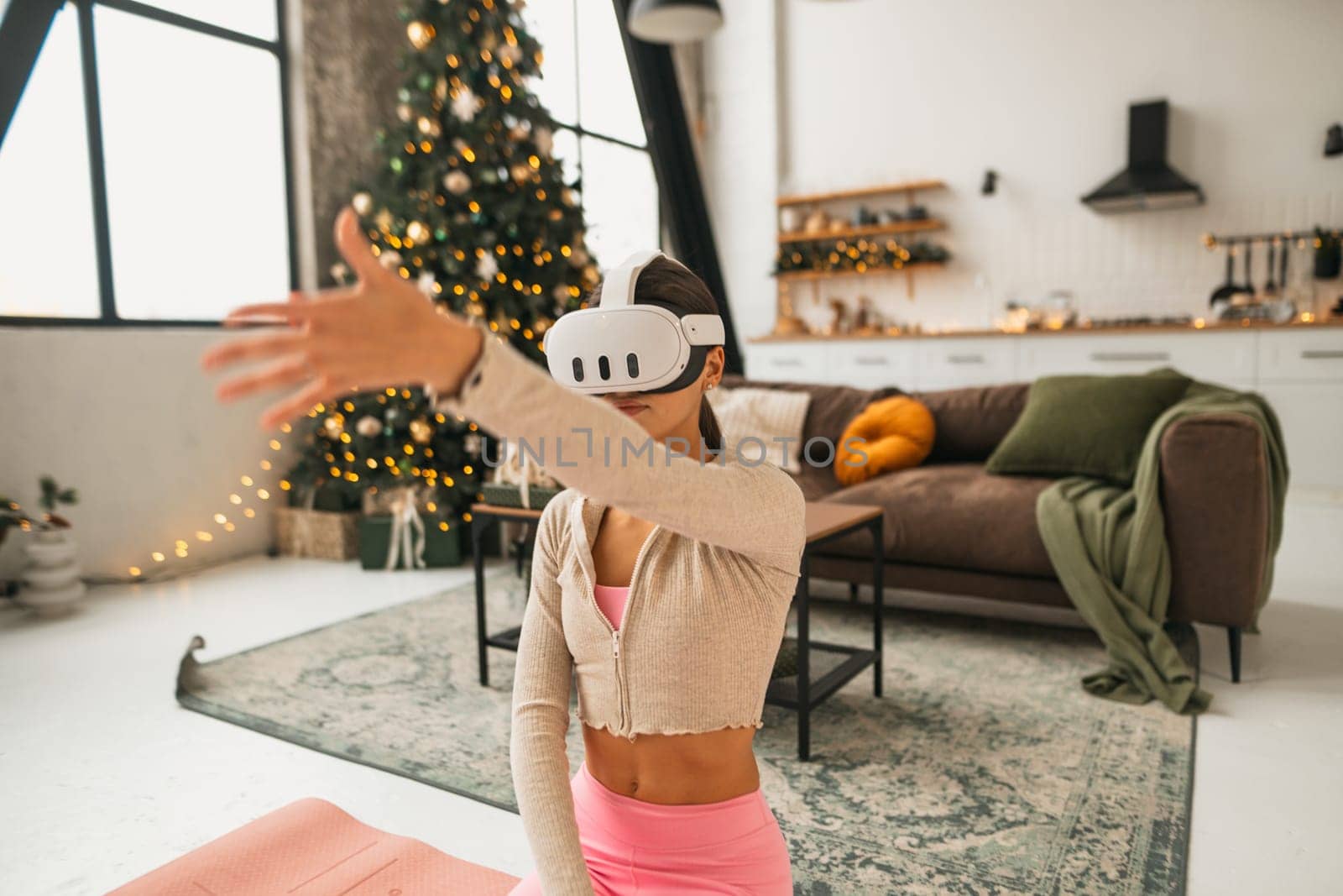 A lovely young lady is seen stretching by a Christmas tree while using virtual reality glasses. High quality photo