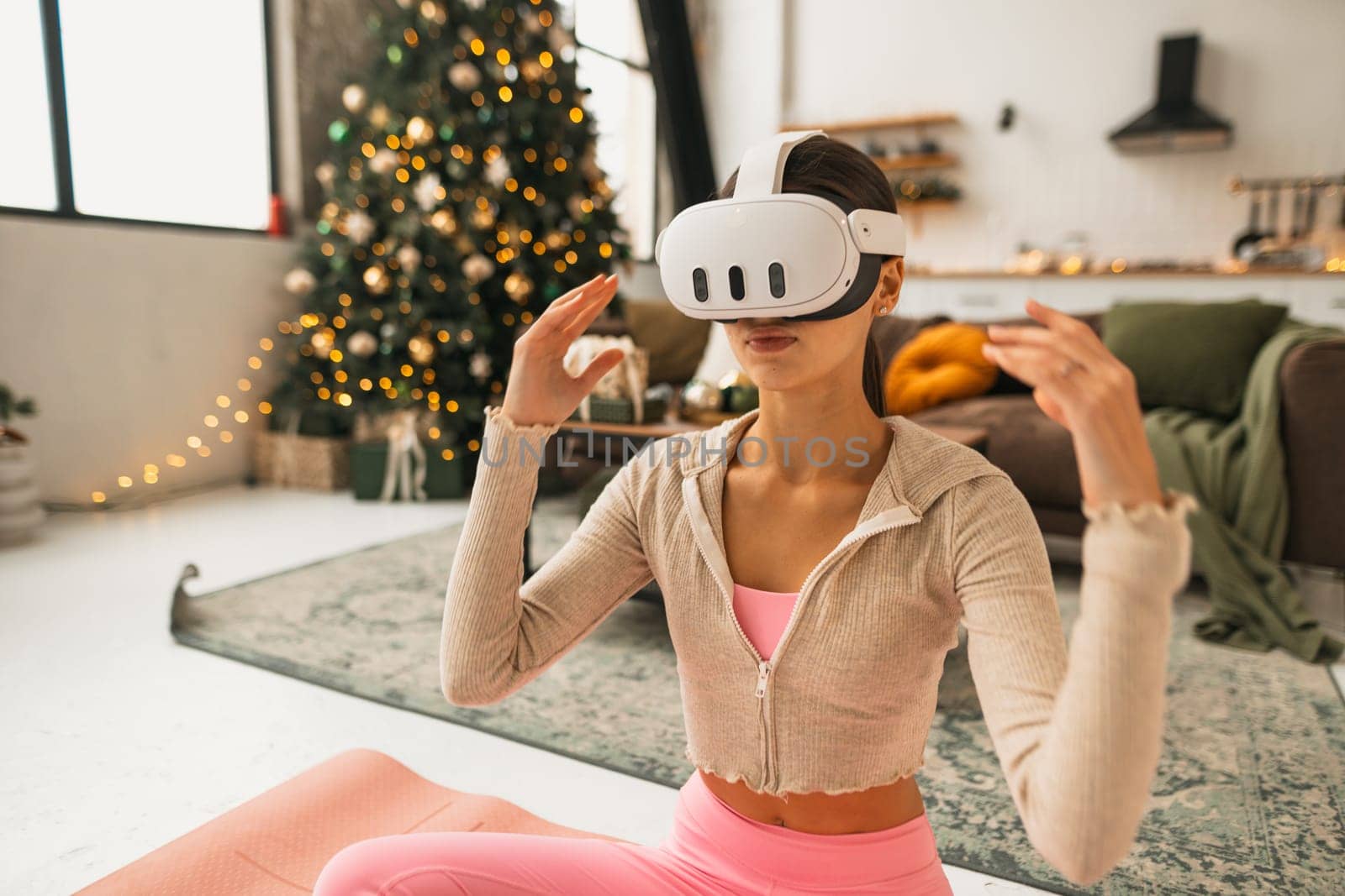 The woman practices yoga wearing pink athletic wear and VR goggles. by teksomolika