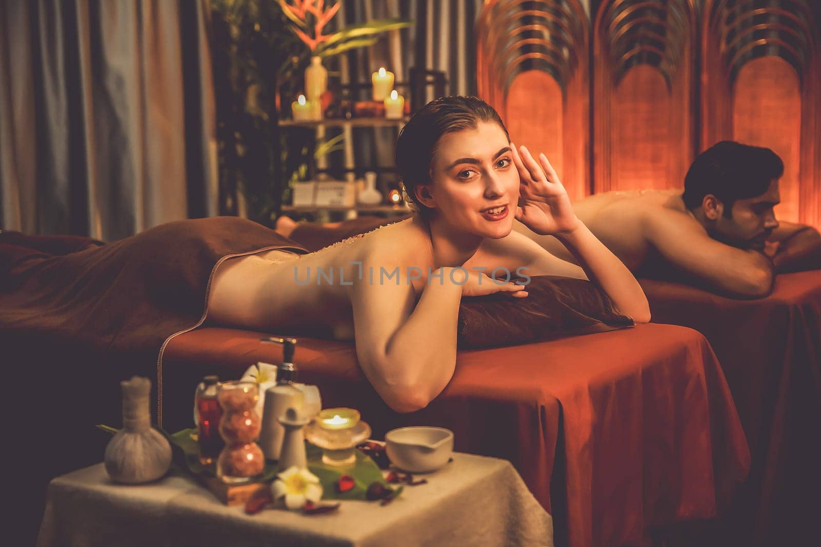 Couple customer having exfoliation treatment in luxury spa salon with warmth candle light ambient. Salt scrub beauty treatment in Health spa body scrub. Quiescent