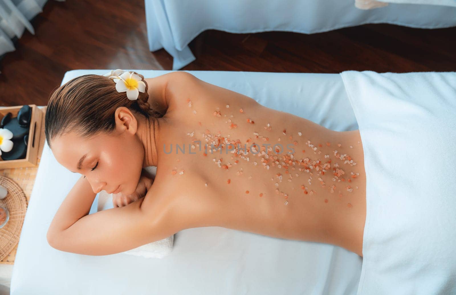 Panorama top view woman customer having exfoliation treatment in luxury spa salon with warmth candle light ambient. Salt scrub beauty treatment in health spa body scrub. Quiescent