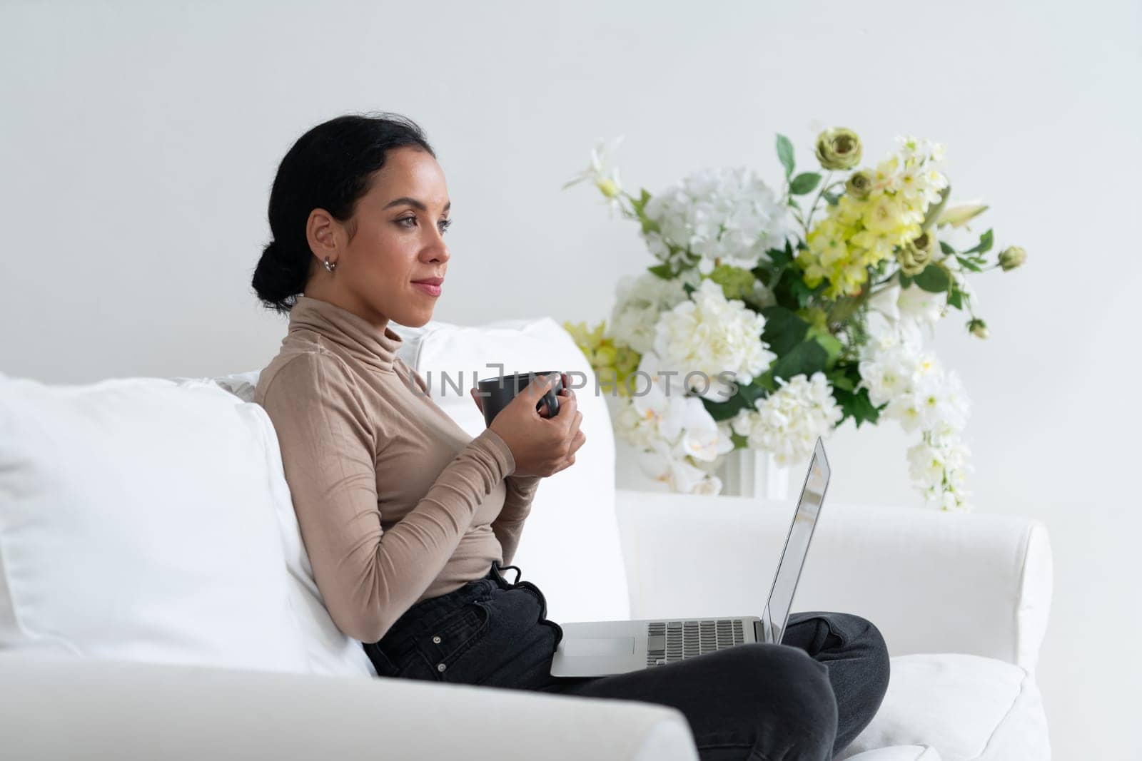 Happy woman drinking coffee on a sofa at home for crucial rest and relaxation. Portrait of young African American woman holding a cup.