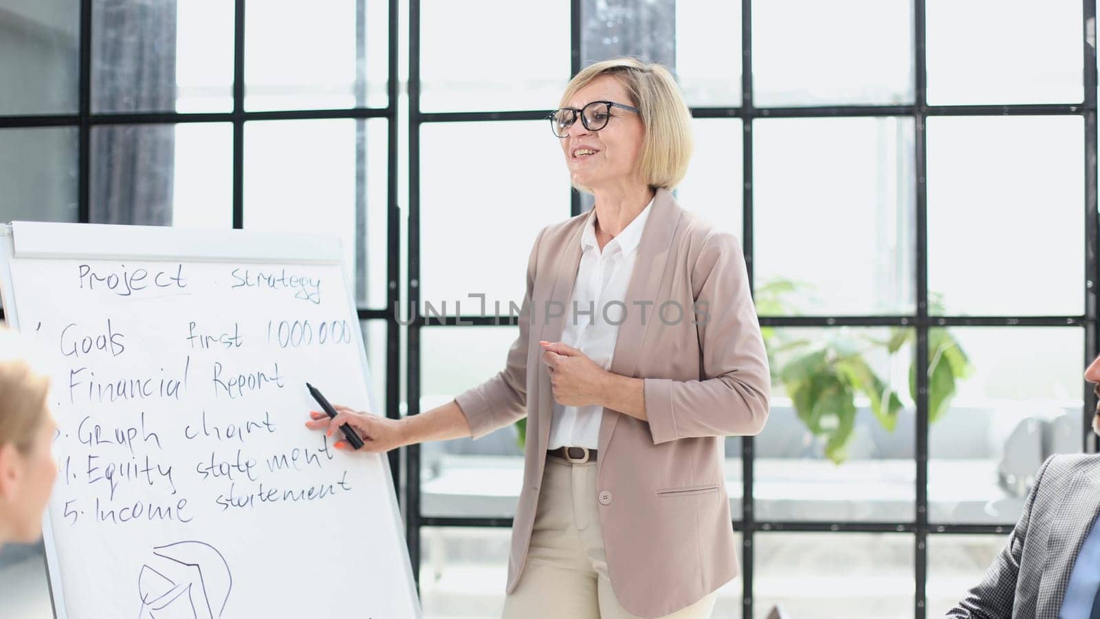Beautiful young businesswoman writing on blank whiteboard in office