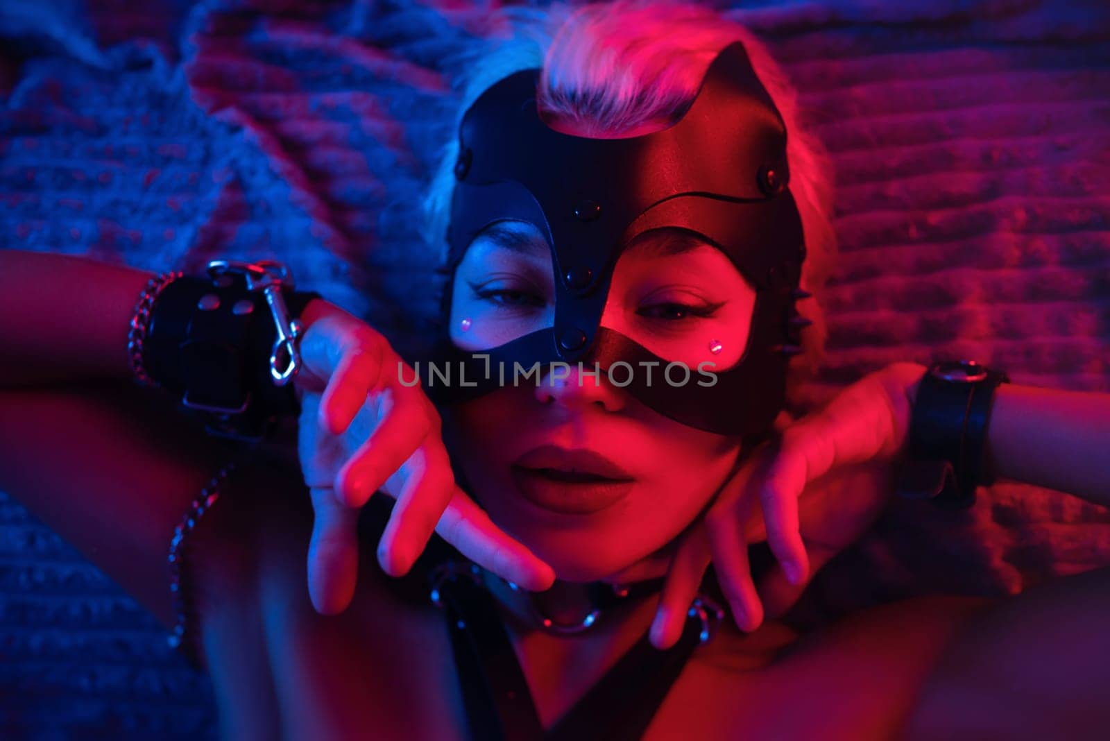 portrait of a sexy girl in a leather mask and bdsm accessories on a bed enjoying sex in orgasm with emotions on her face in neon light by Rotozey