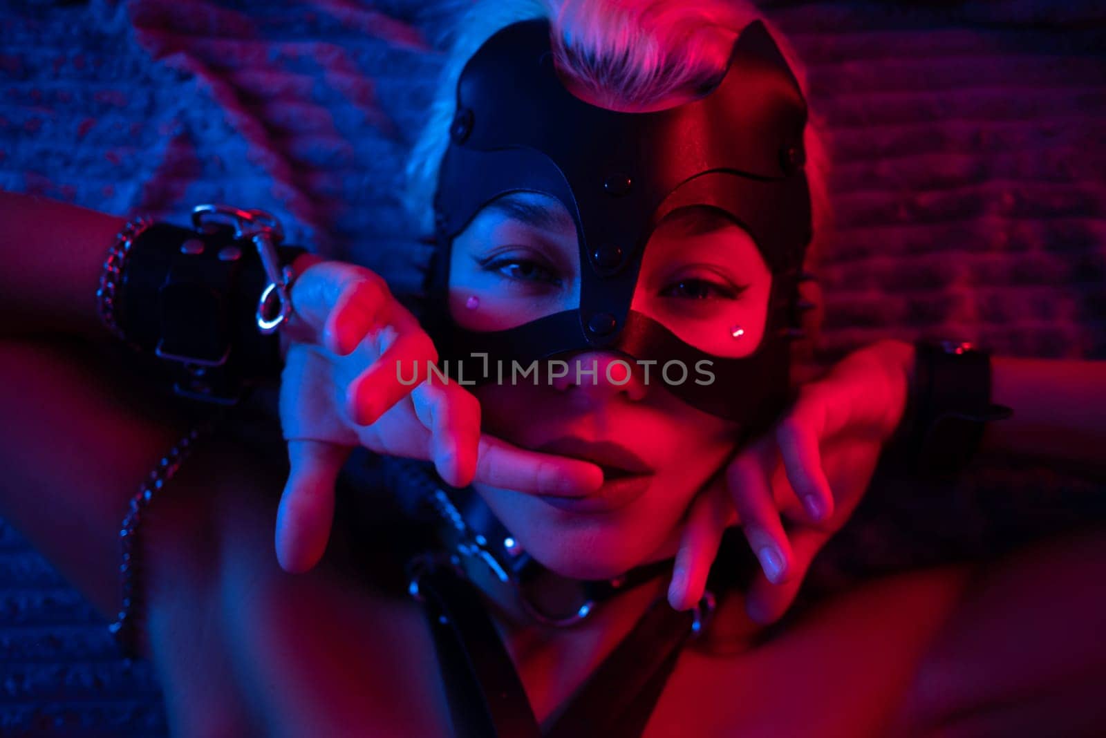 portrait of a sexy girl in a leather mask and bdsm accessories on a bed enjoying sex in orgasm with emotions on her face in neon light by Rotozey