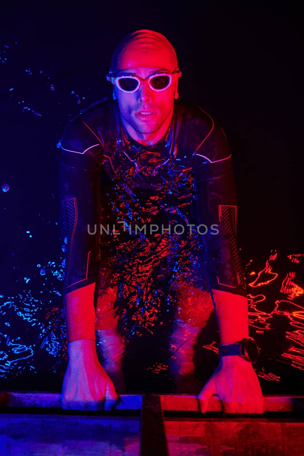 real triathlete swimmer having a break during hard training at lake on dark night neon gel color lights