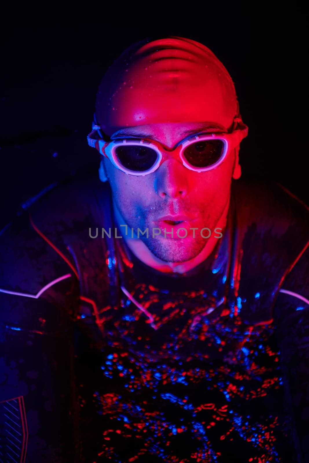 real triathlete swimmer having a break during hard training at lake on dark night neon gel color lights