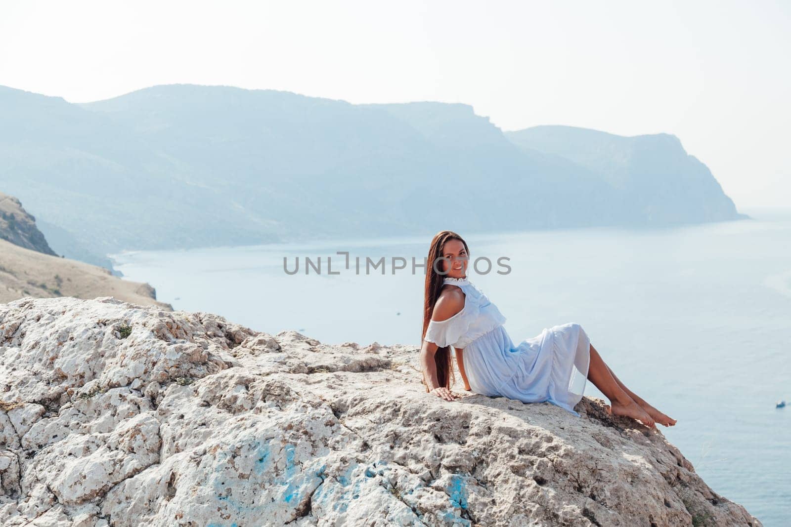 A woman with long hair in a dress looks at the landscape of the sea and rocks