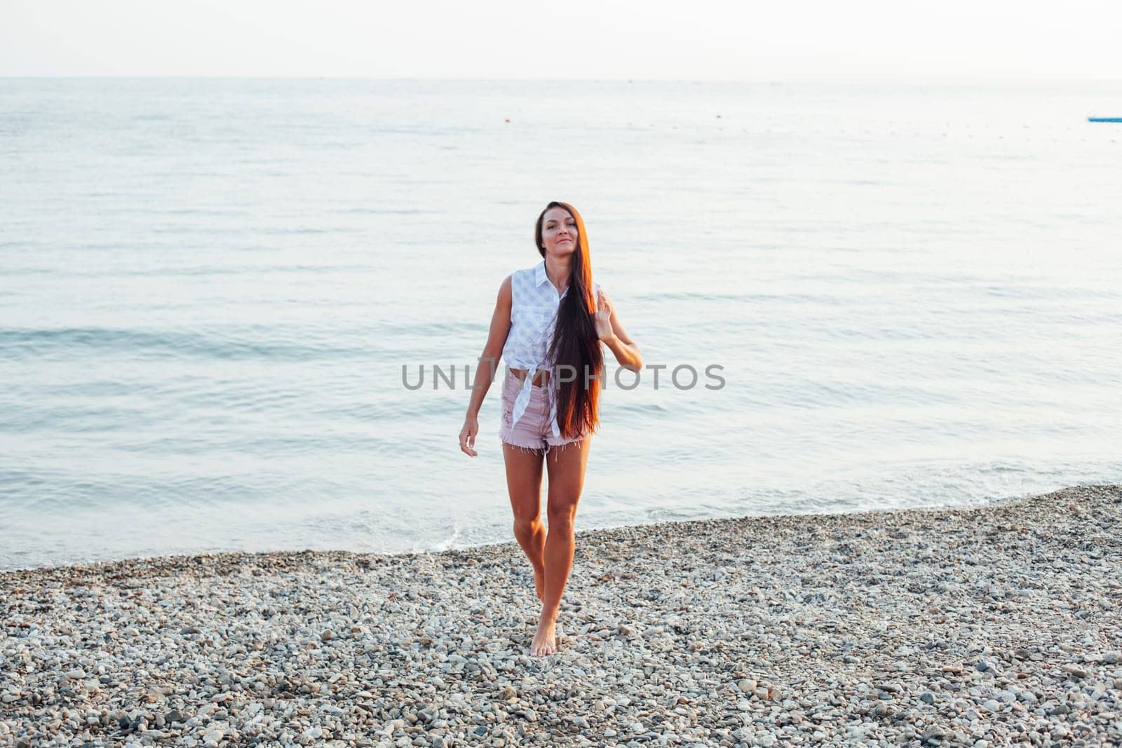 Beautiful tanned woman with long hair walks on the beach by the sea by Simakov