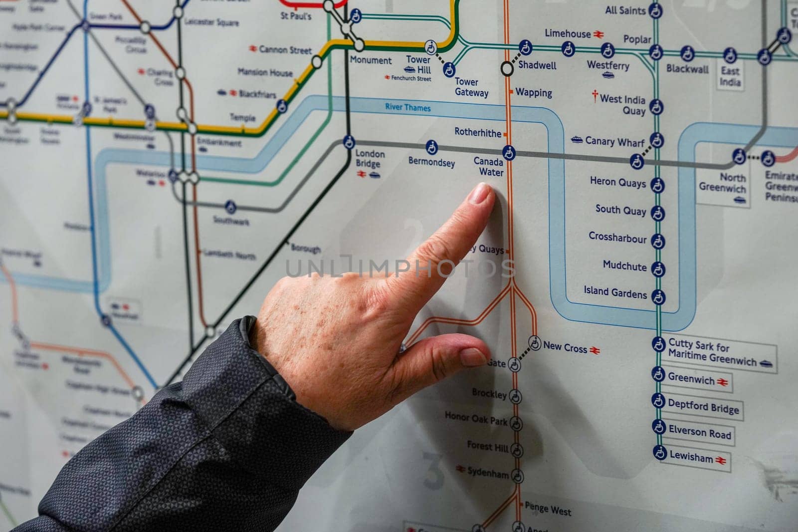 London, United Kingdom - February 02, 2019: Senior woman hand pointing to Canada Water station on London Tube map, as she plans her journey. Underground railway in UK capital serves 270 stations