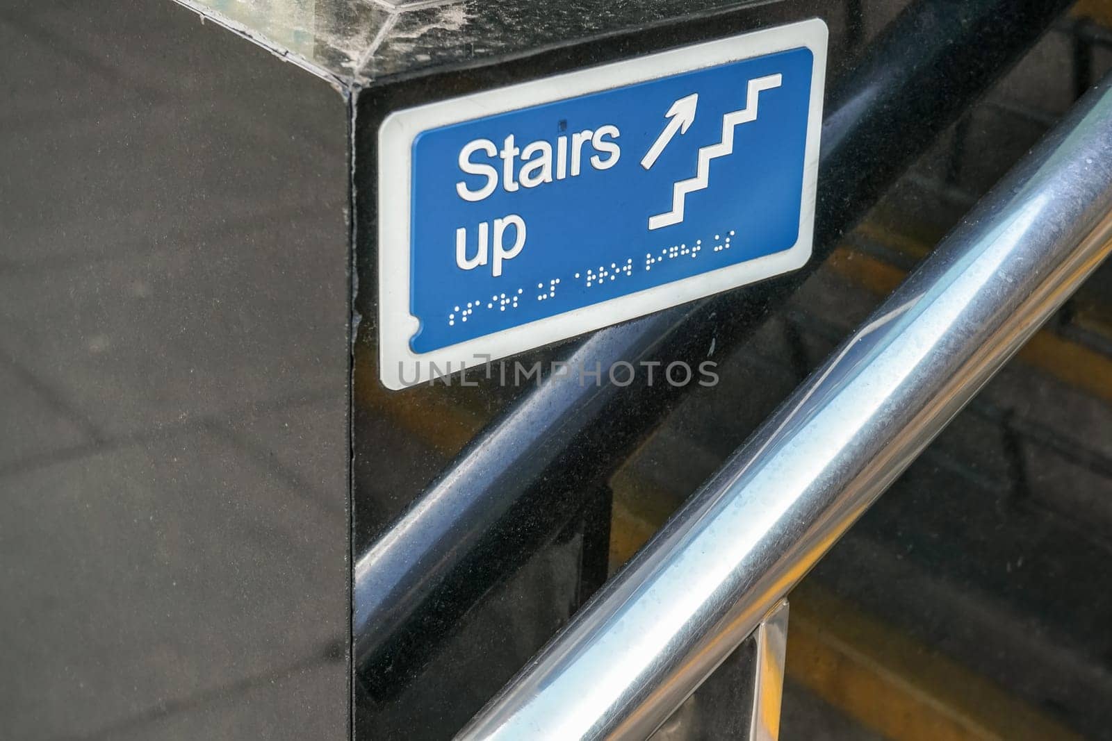 Detail on blue "Stairs up" sign with writing in Braille for blind disabled people below.