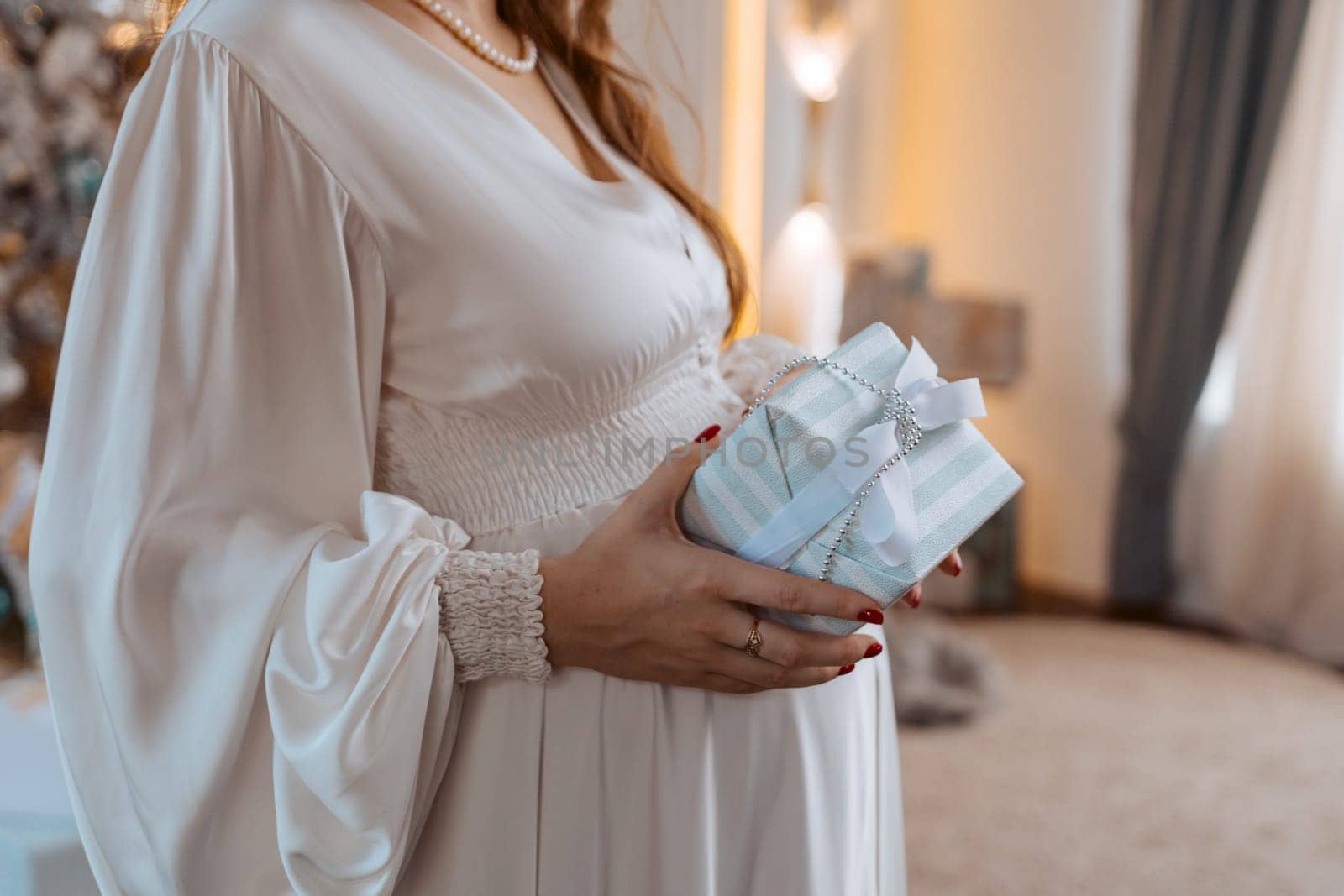 Pregnant woman holds a gift on her stomach against Christmas tree with lights. family holiday concept Christmas holidays