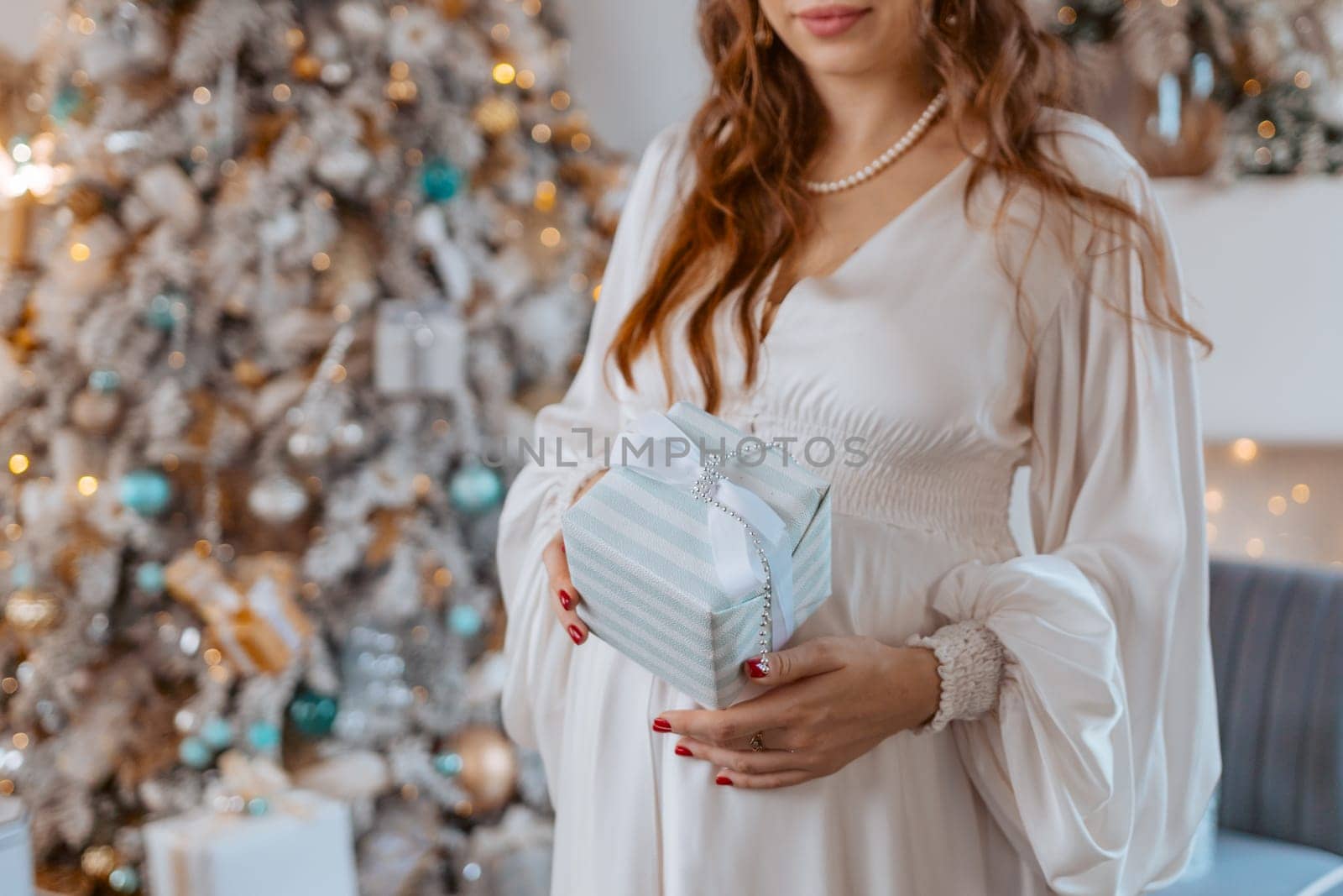Pregnant woman holds a gift on her stomach against Christmas tree with lights. family holiday concept Christmas holidays
