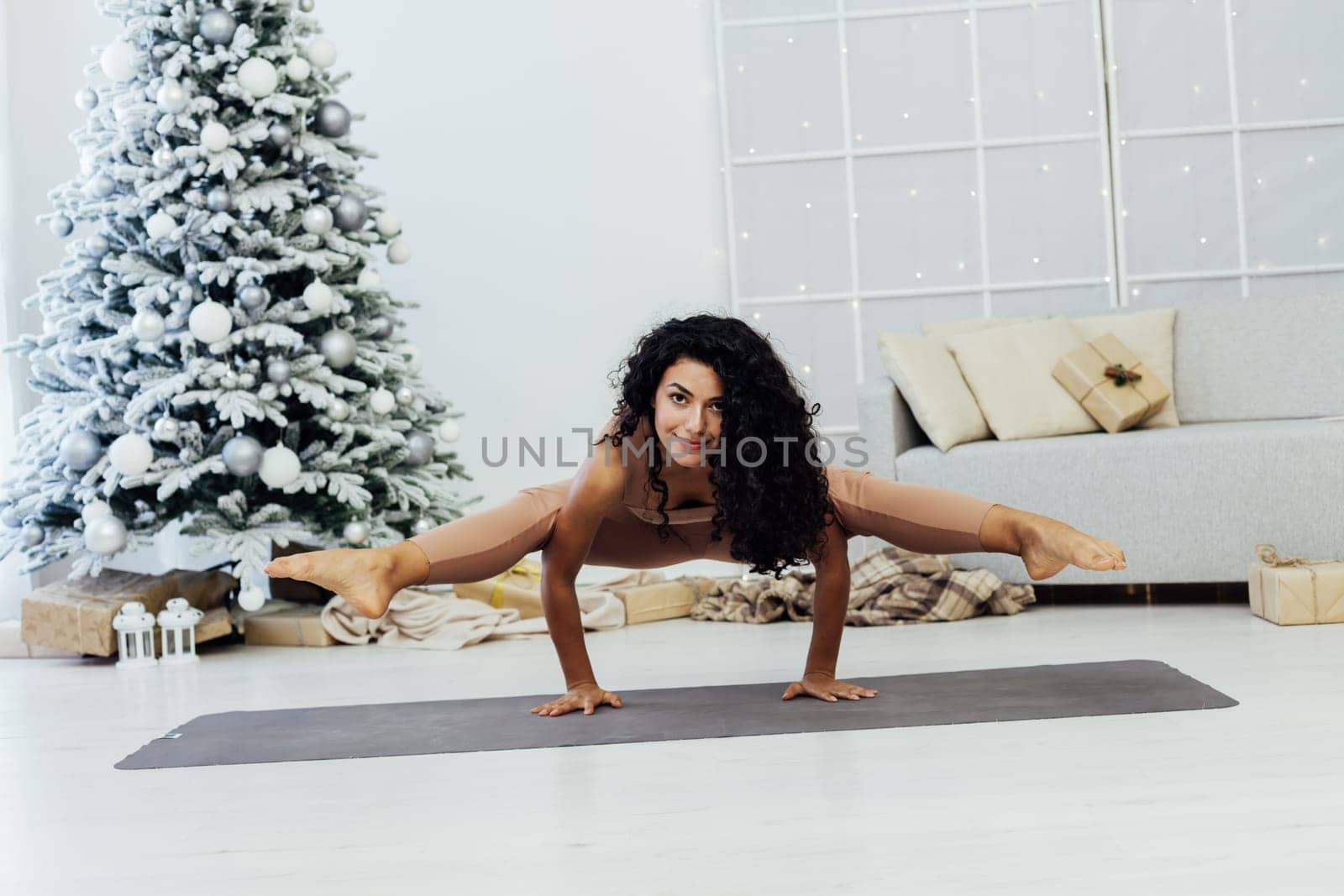 Beautiful brunette woman engaged in yoga fitness gymnastics asana near christmas tree