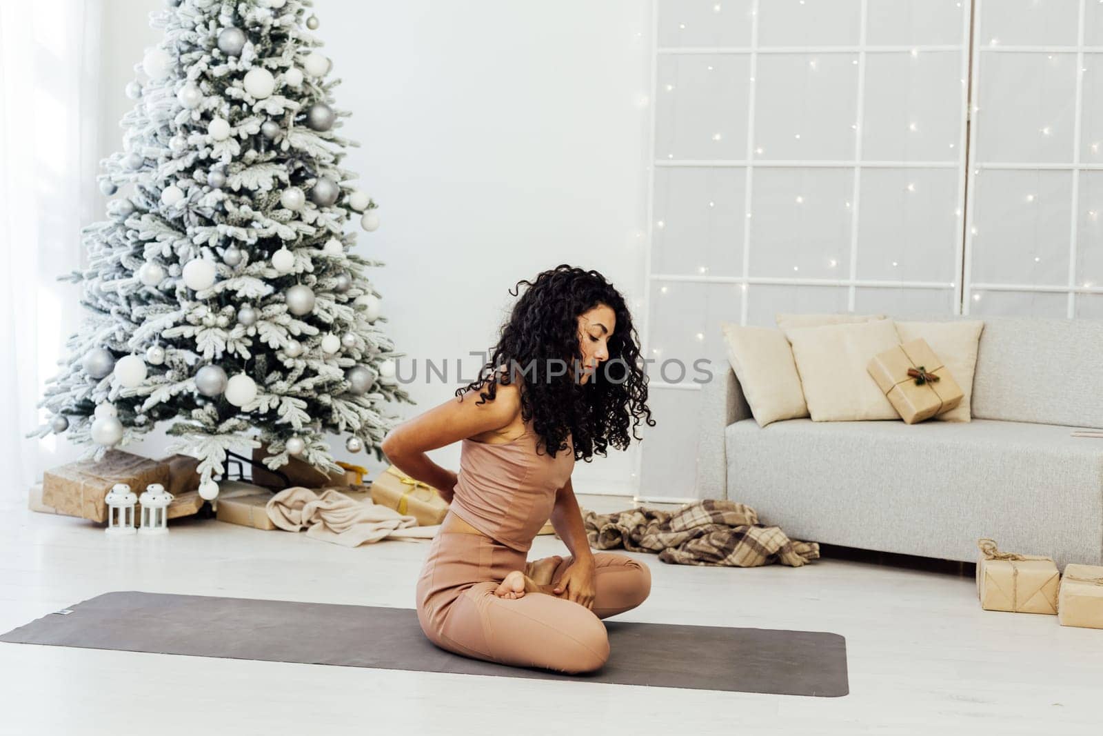 Beautiful brunette woman engaged in yoga fitness gymnastics asana near christmas tree