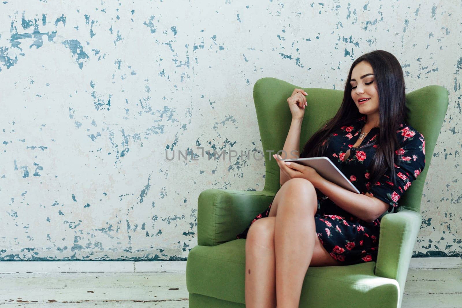 Portrait of a beautiful fashionable woman in a black dress with flowers with an internet tablet in a chair