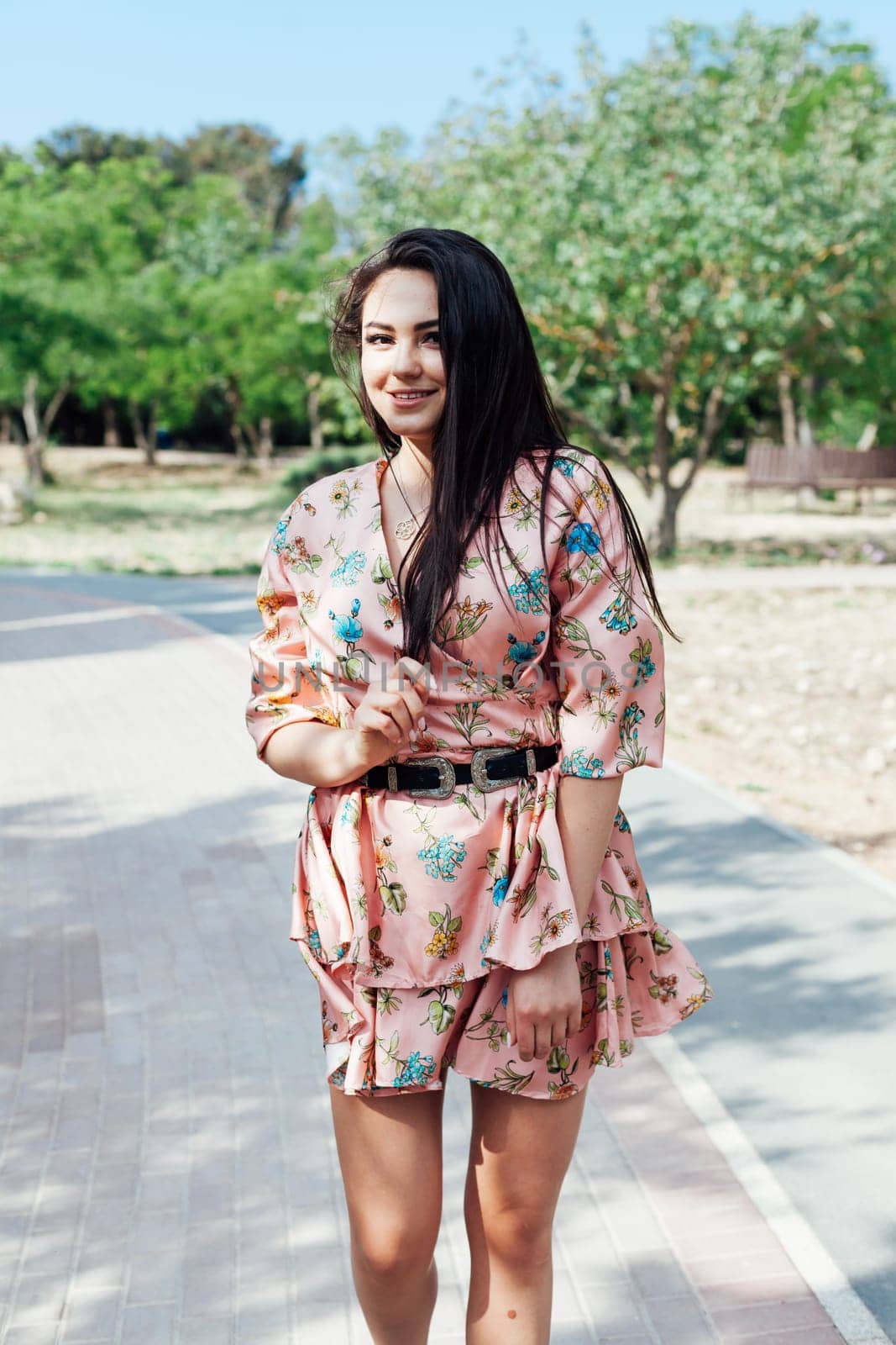 Beautiful athletic woman in dress with flowers walks in park alone