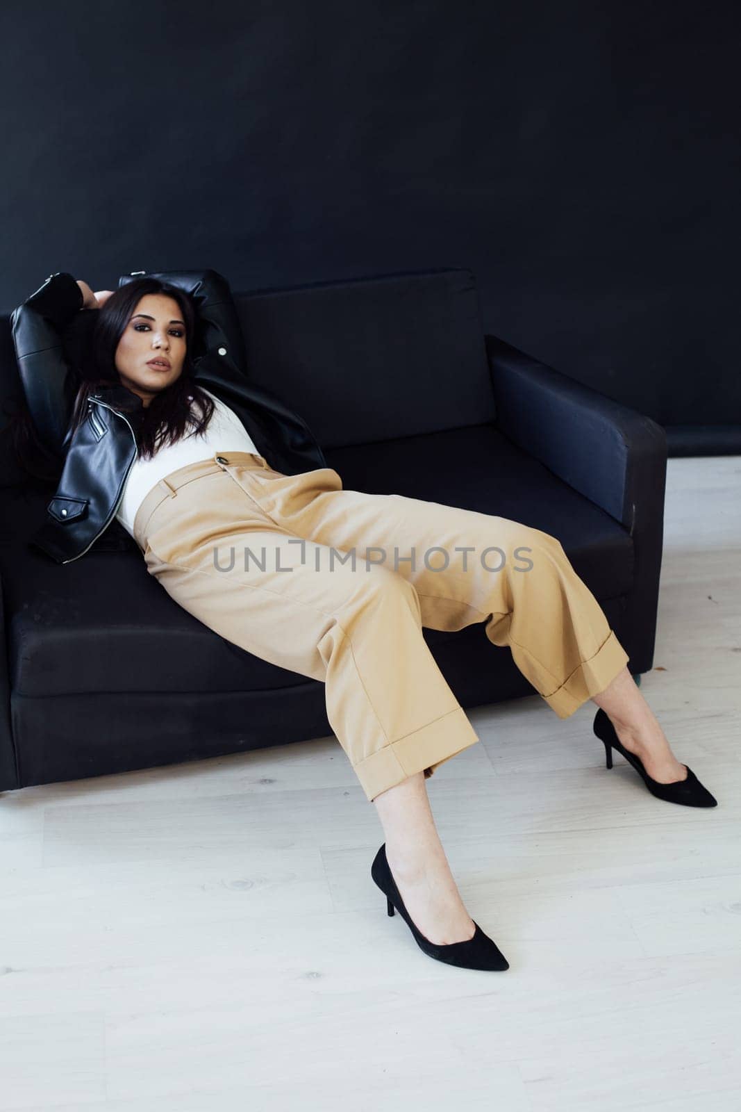 Portrait of a beautiful fashionable brunette woman on a home black sofa by Simakov