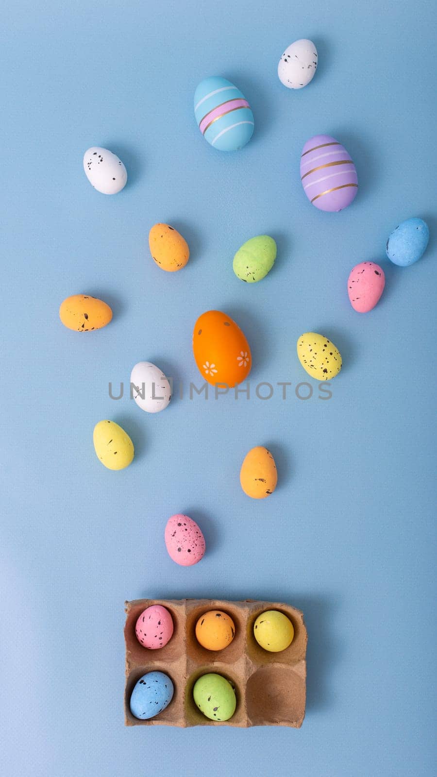 Beautiful decorative multicolored eggs are scattered on a light blue background, top view.