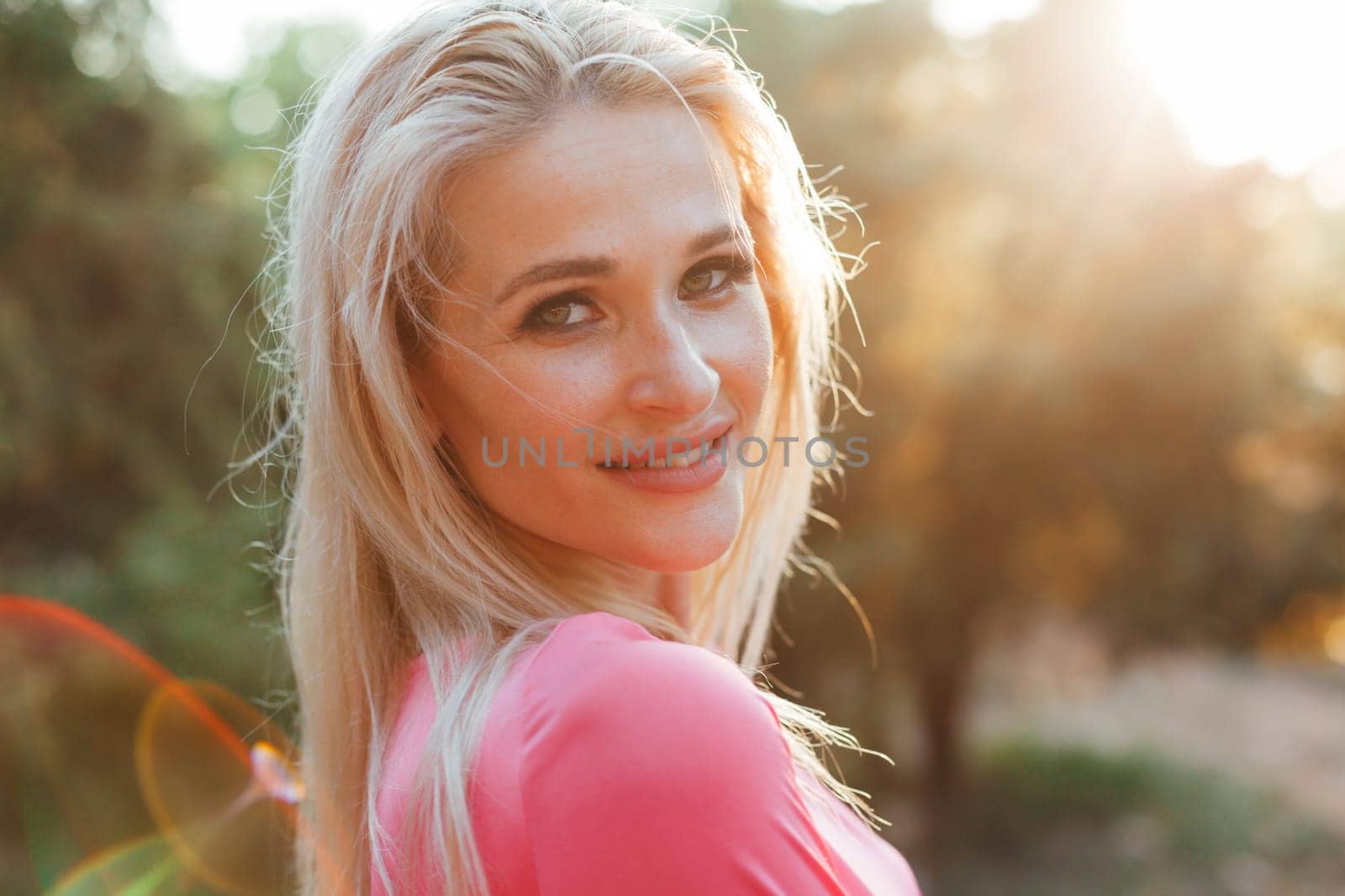 Beautiful woman in pink dress walks in the park at sunset
