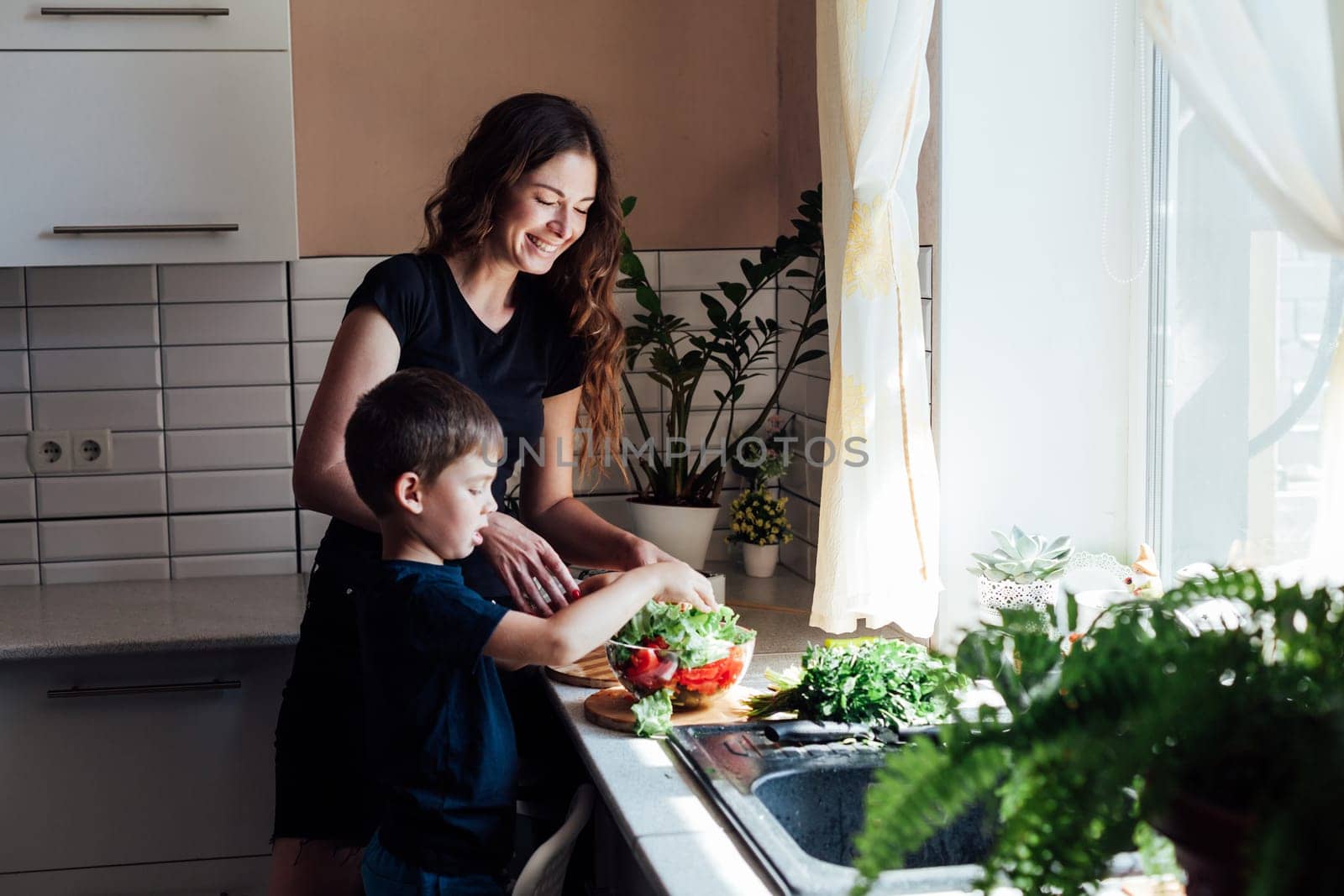 Mom and young son cut ripe vegetables for salad in the kitchen