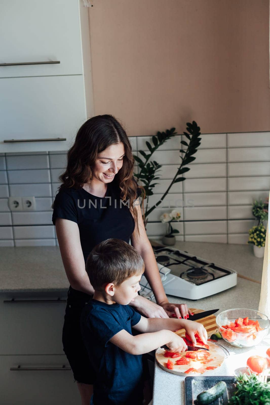 Mom and young son cut vegetables for salad in the kitchen by Simakov