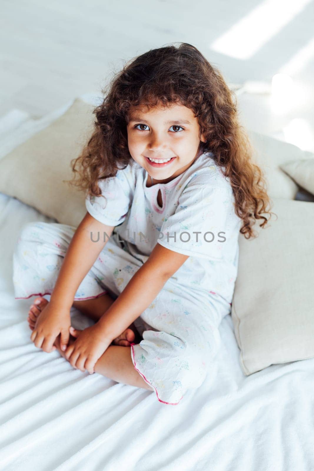 curly girl in pajamas sits on bed in bedroom