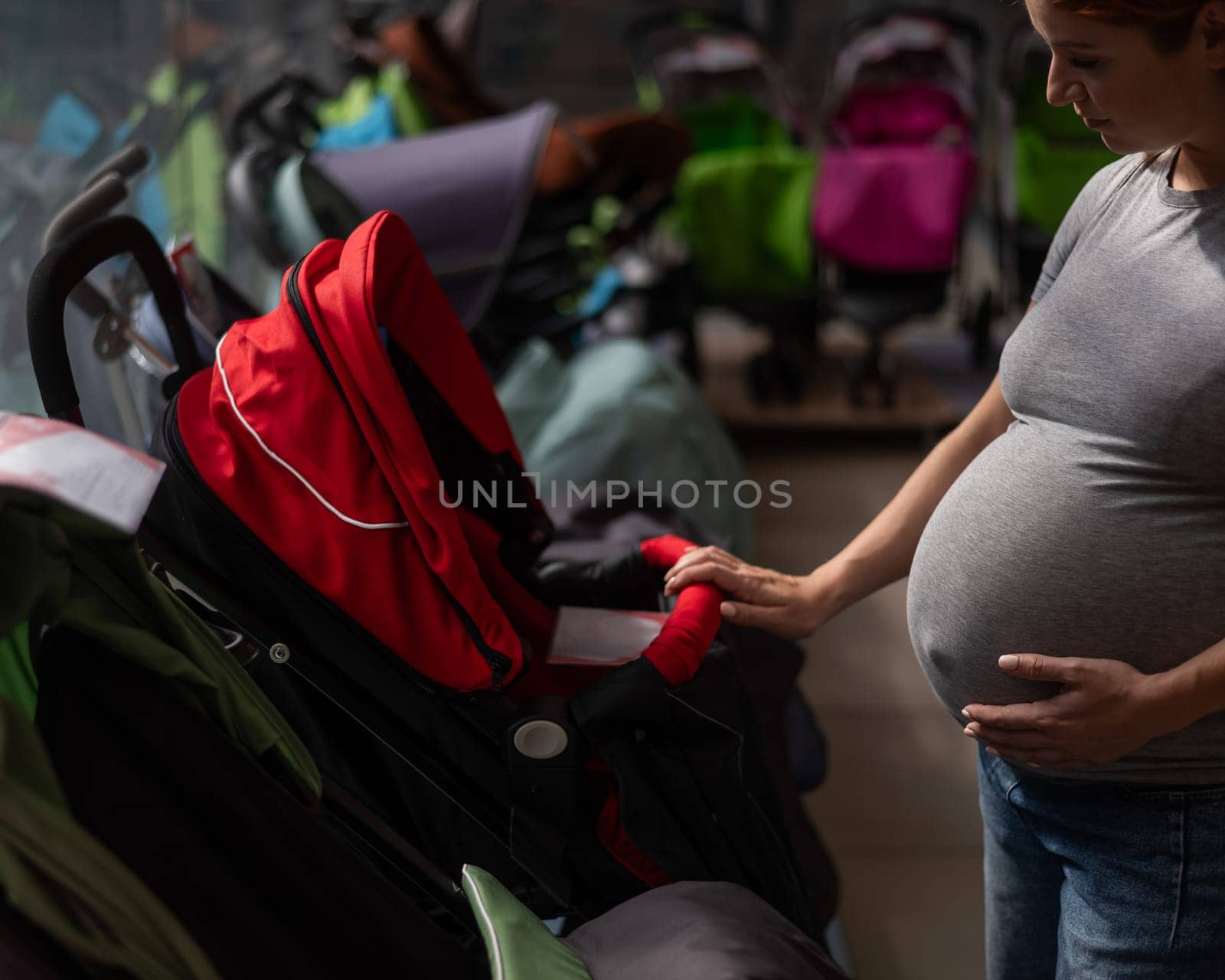Red-haired pregnant woman chooses a stroller in a children's store. by mrwed54