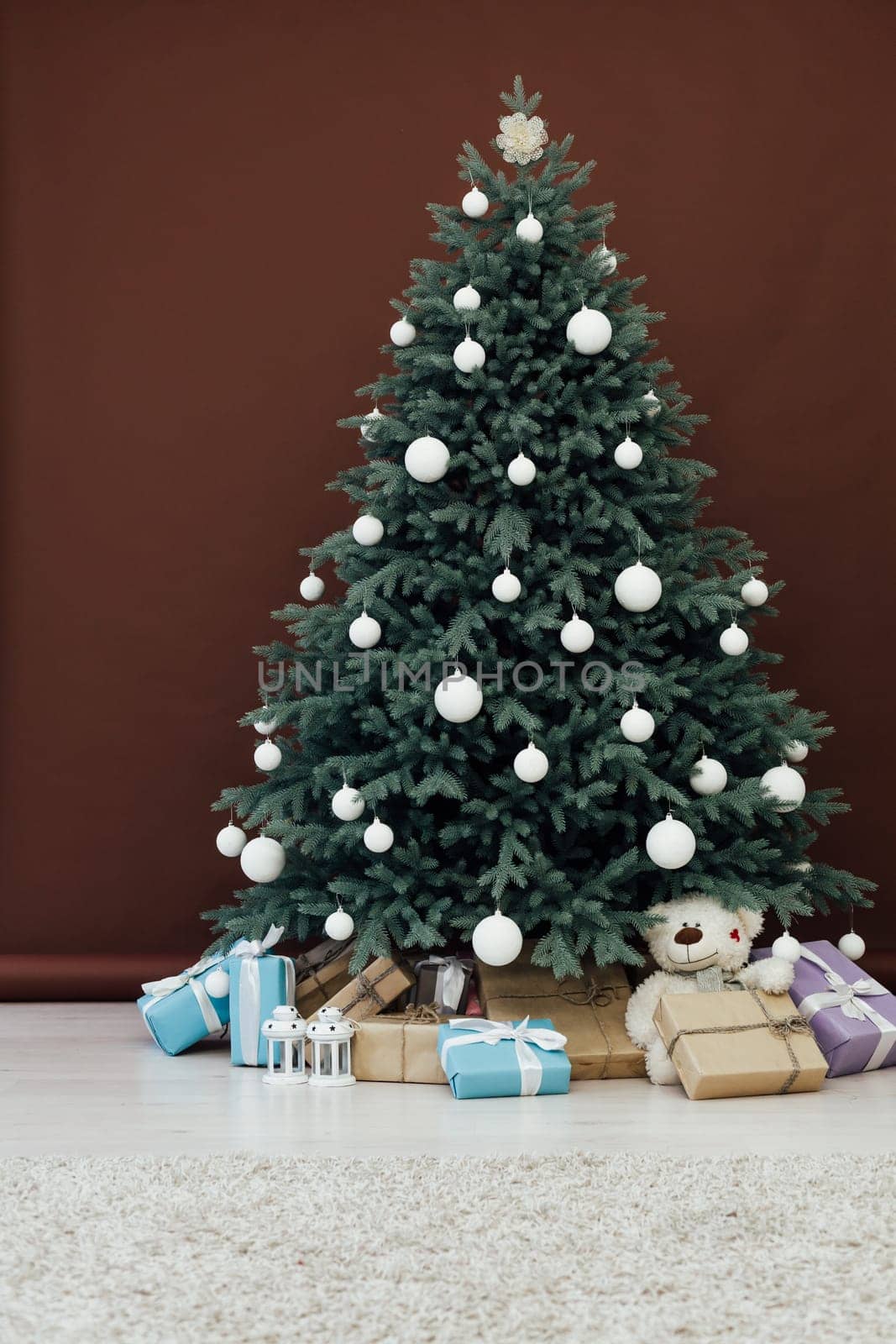 Christmas tree with presents underneath in living room. White room. Bright lights and bokeh.