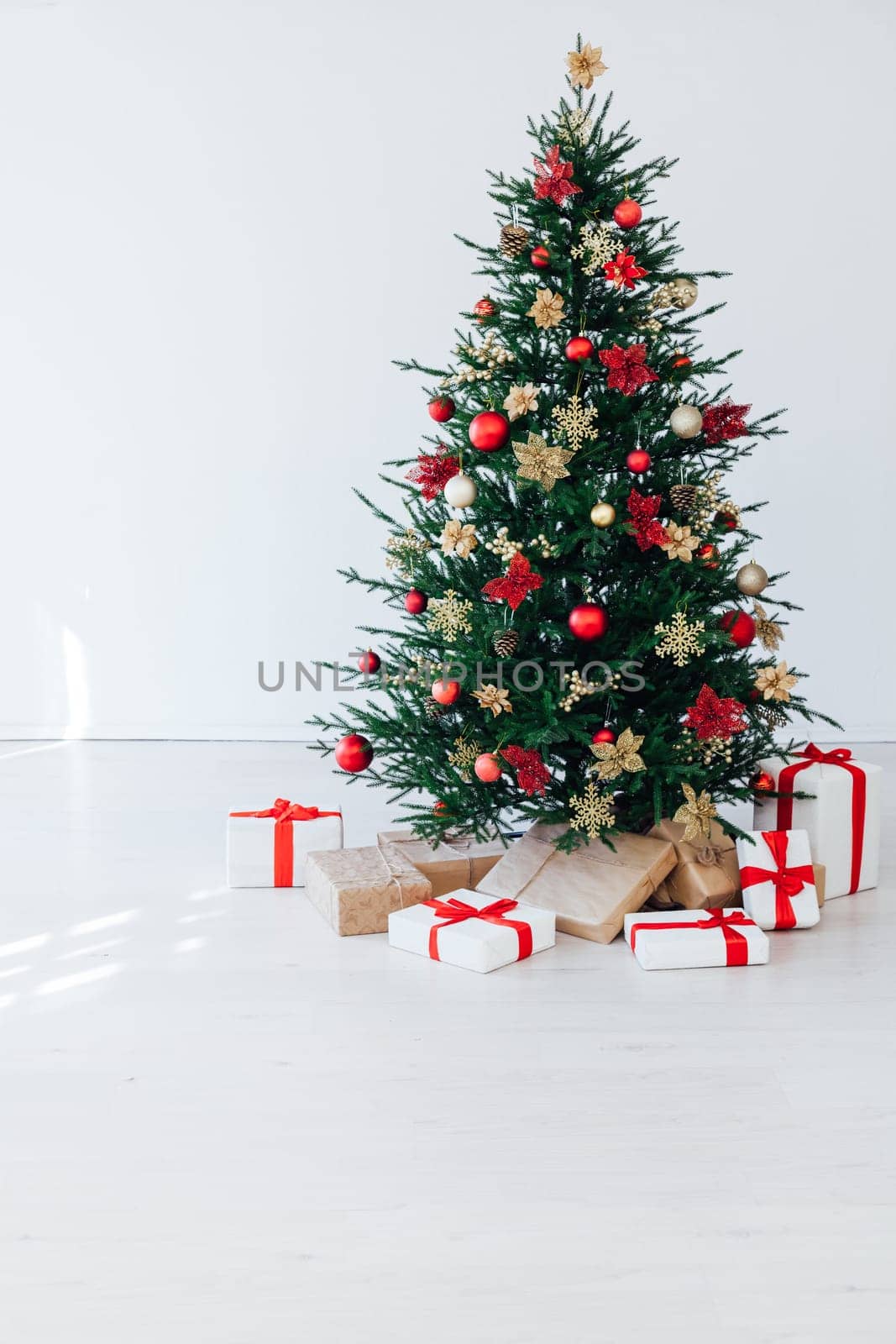 christmas tree with colorful balls and gift boxes over white brick wall