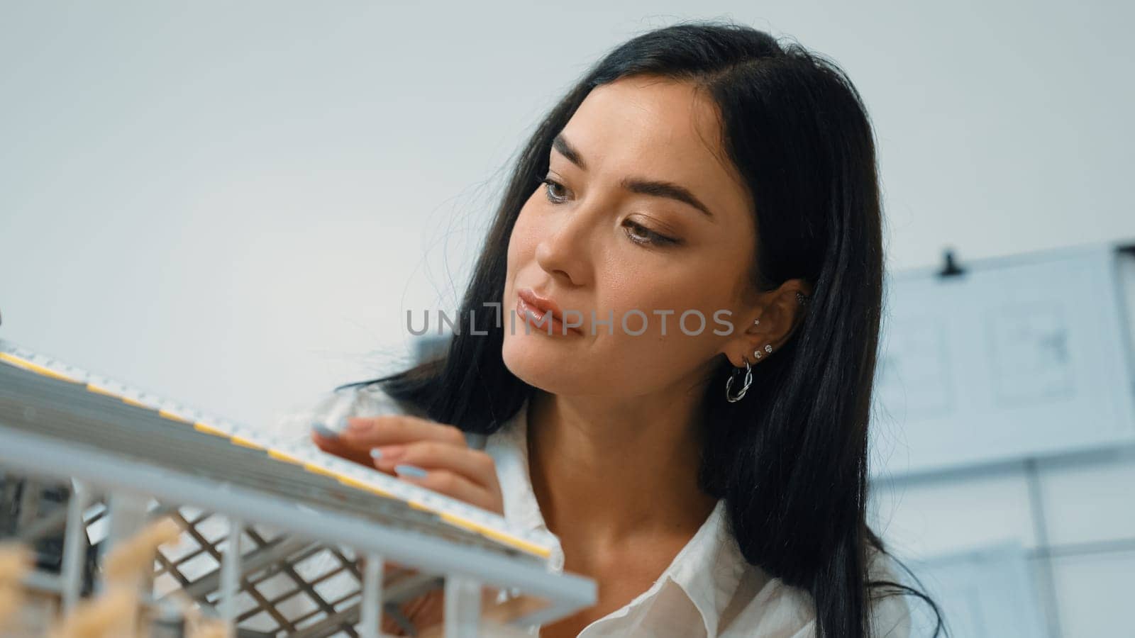 Professional young beautiful architect engineer using ruler and pencil measuring model roof length at modern office with blueprint pinned behind. Creative design and living concept. Immaculate.