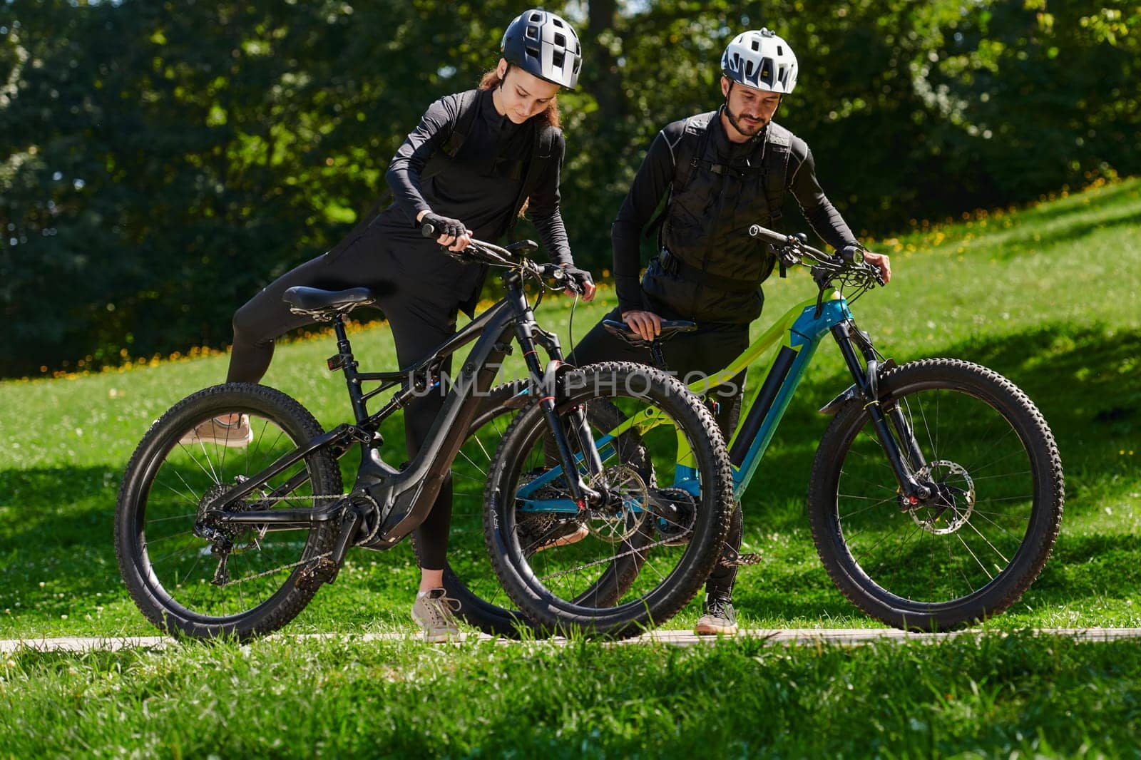 A sweet couple, equipped with bicycles and engrossed in coordinating their journey, checks their GPS mobile and watches while planning scenic routes in the park, seamlessly blending technology and outdoor adventure for a delightful cycling experience by dotshock