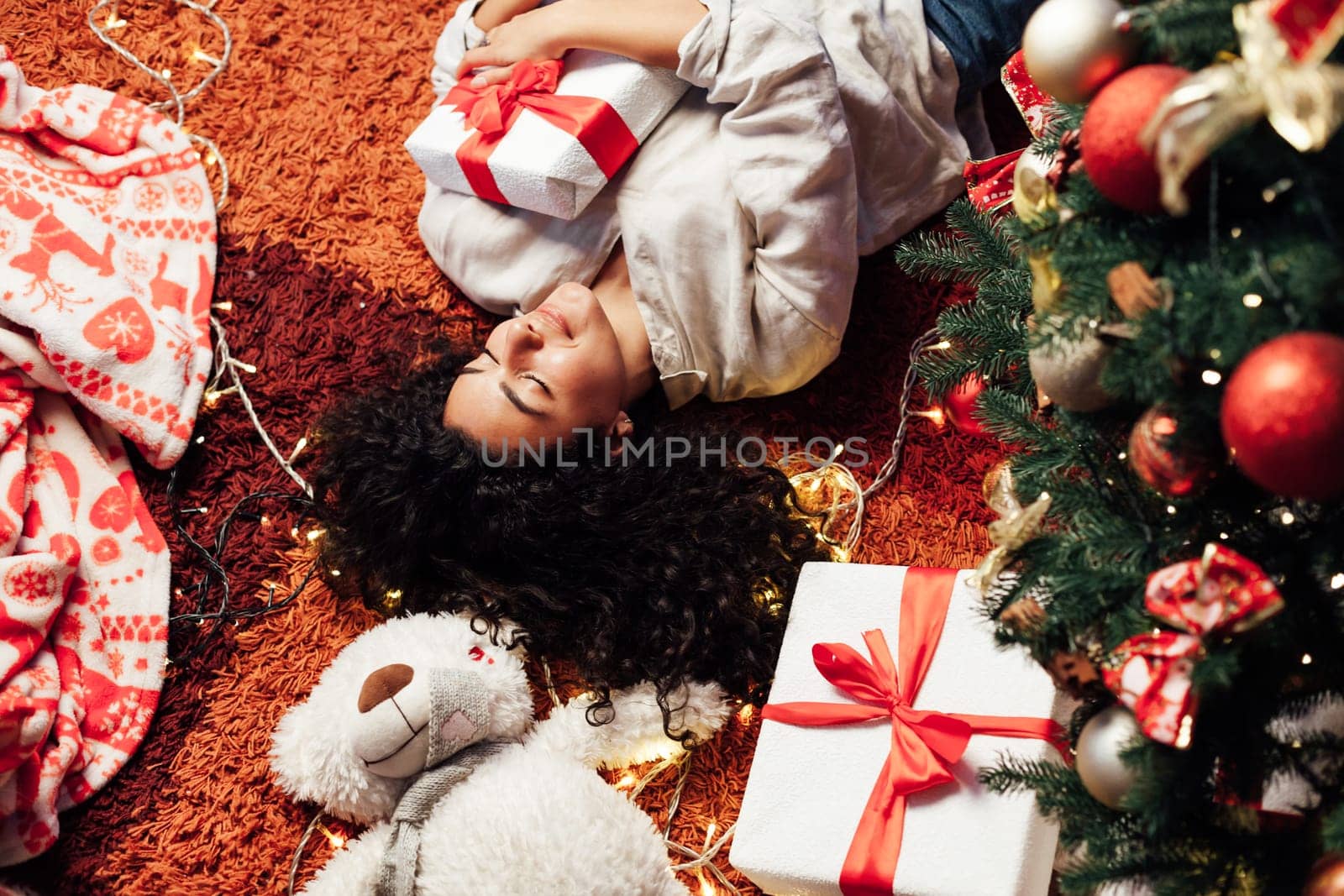 Beautiful brunette woman lies near Christmas tree opens gifts for new year by Simakov
