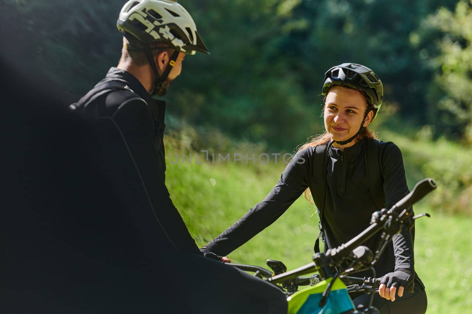 A sweet couple, equipped with bicycles and engrossed in coordinating their journey, checks their GPS mobile and watches while planning scenic routes in the park, seamlessly blending technology and outdoor adventure for a delightful cycling experience by dotshock