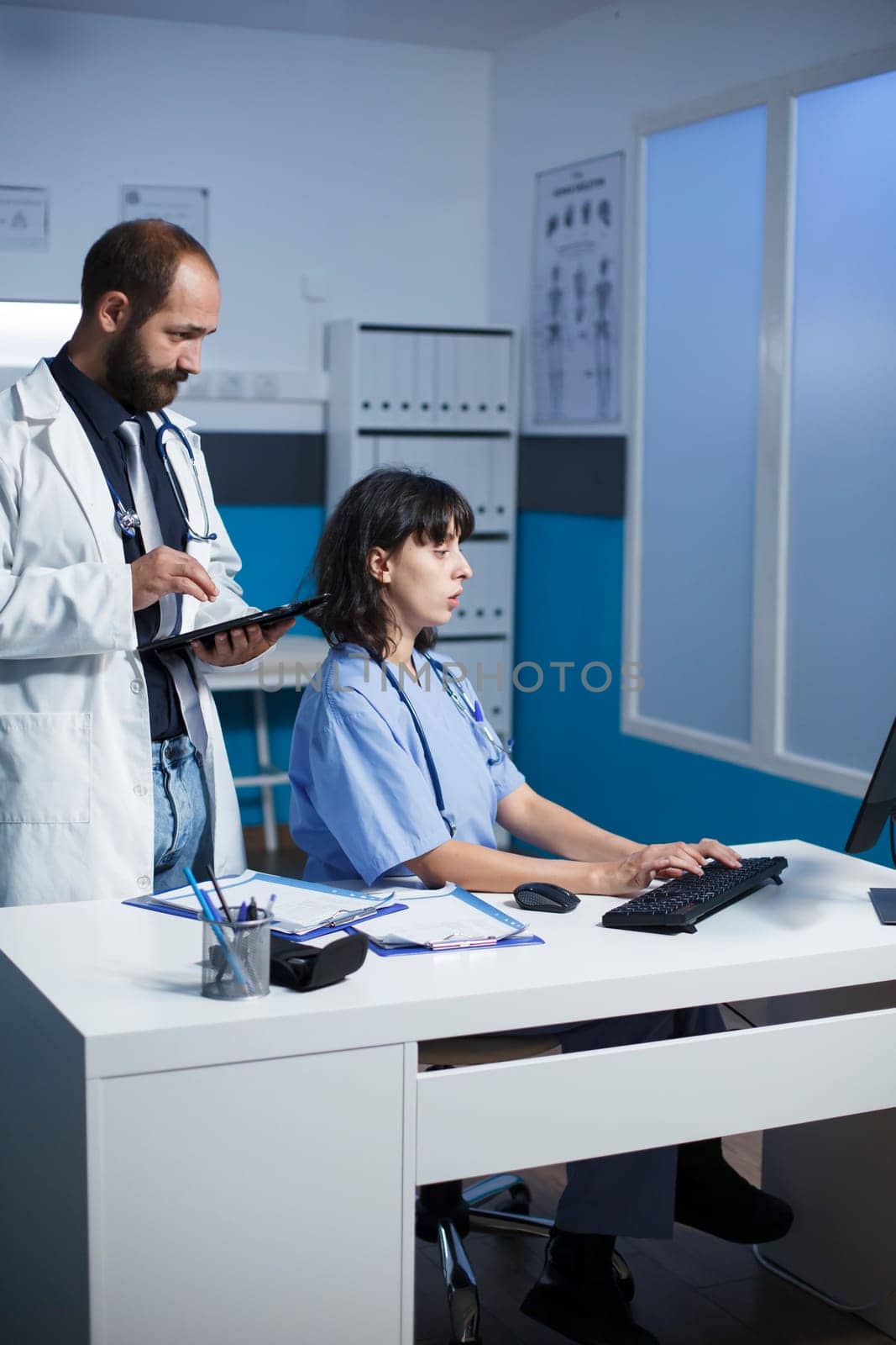 Caucasian doctor and female healthcare worker collaborating in a hospital office. They discuss medical cases, using digital devices for communication and showing images on a tablet.