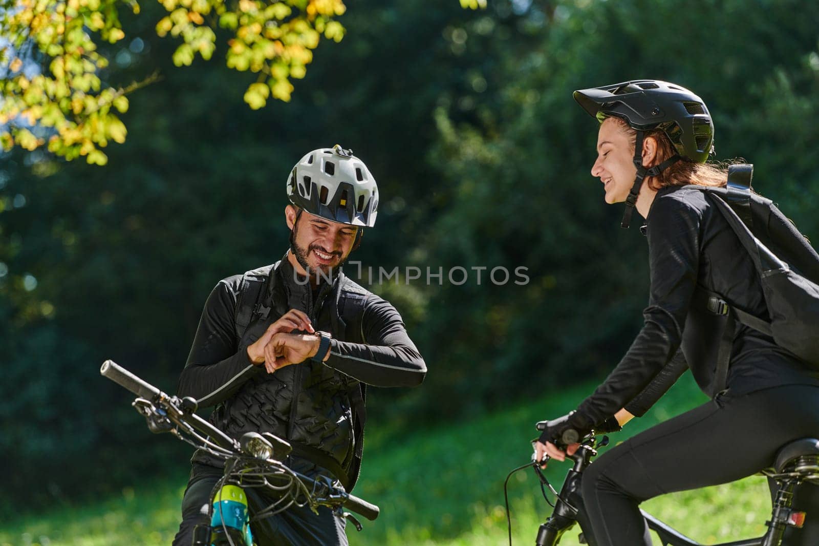 A sweet couple, equipped with bicycles and engrossed in coordinating their journey, checks their GPS mobile and watches while planning scenic routes in the park, seamlessly blending technology and outdoor adventure for a delightful cycling experience by dotshock