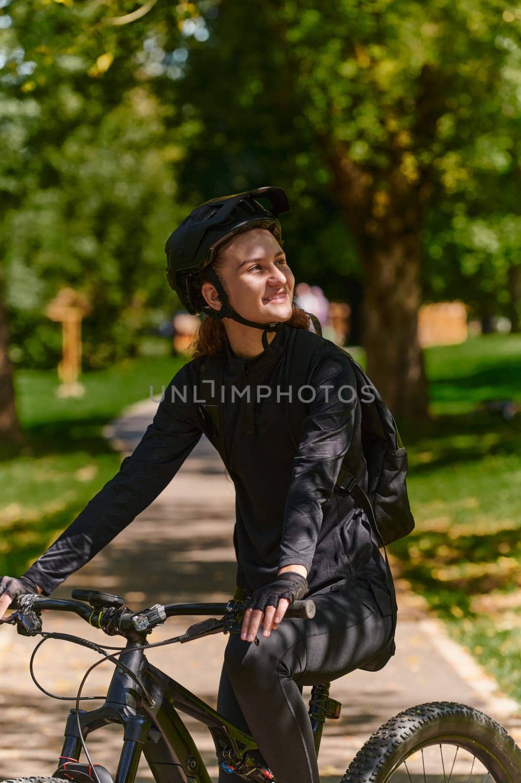 In the radiant embrace of a sunny day, a modern woman revels in the joy of cycling, her sleek bicycle and professional gear complementing her active lifestyle as she rides through the park, epitomizing a perfect blend of style and outdoor vitality.