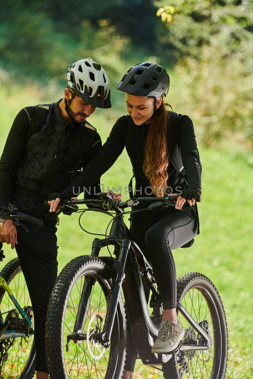 A blissful couple, adorned in professional cycling gear, enjoys a romantic bicycle ride through a park, surrounded by modern natural attractions, radiating love and happiness.