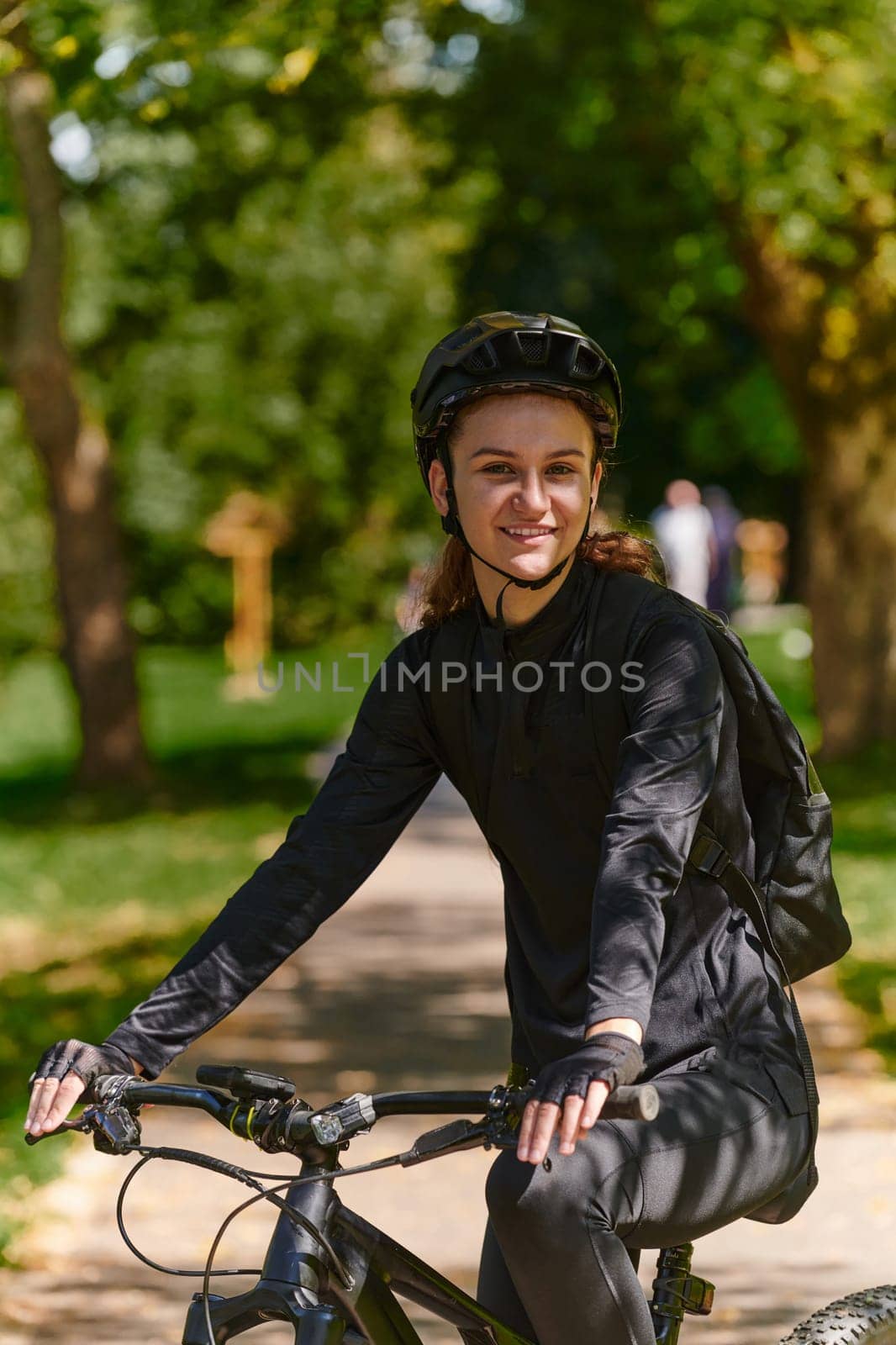 In the radiant embrace of a sunny day, a modern woman revels in the joy of cycling, her sleek bicycle and professional gear complementing her active lifestyle as she rides through the park, epitomizing a perfect blend of style and outdoor vitality.