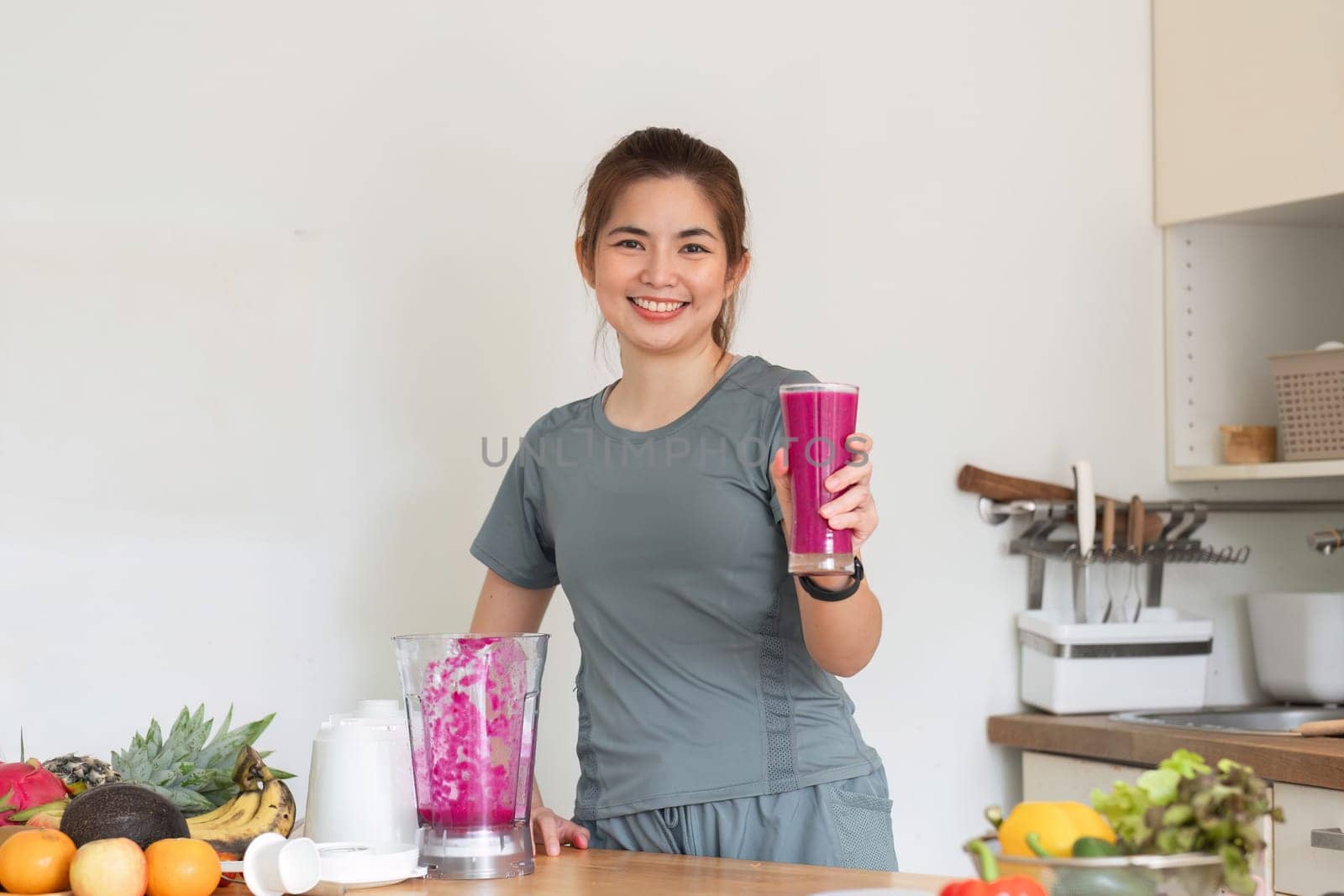 Young attractive Asian woman makes a fruit smoothie in the kitchen. Take care of your health by eating fruits and vegetables to add vitamins..