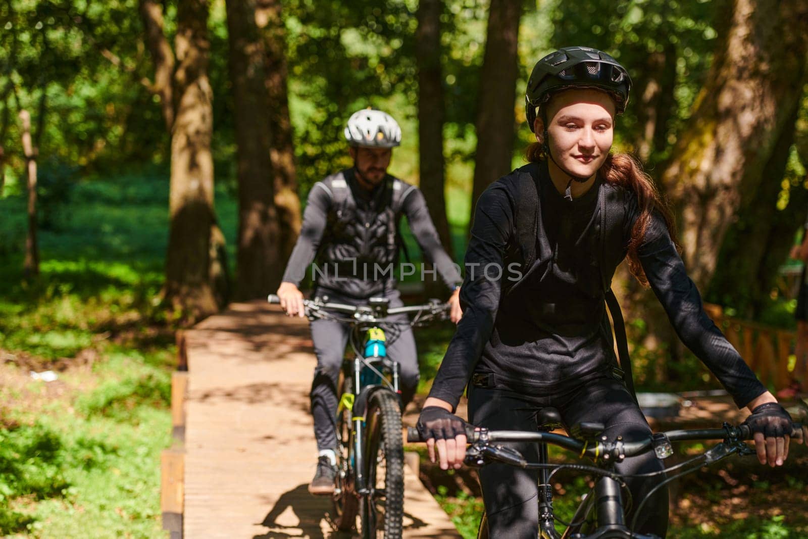 A blissful couple, adorned in professional cycling gear, enjoys a romantic bicycle ride through a park, surrounded by modern natural attractions, radiating love and happiness.