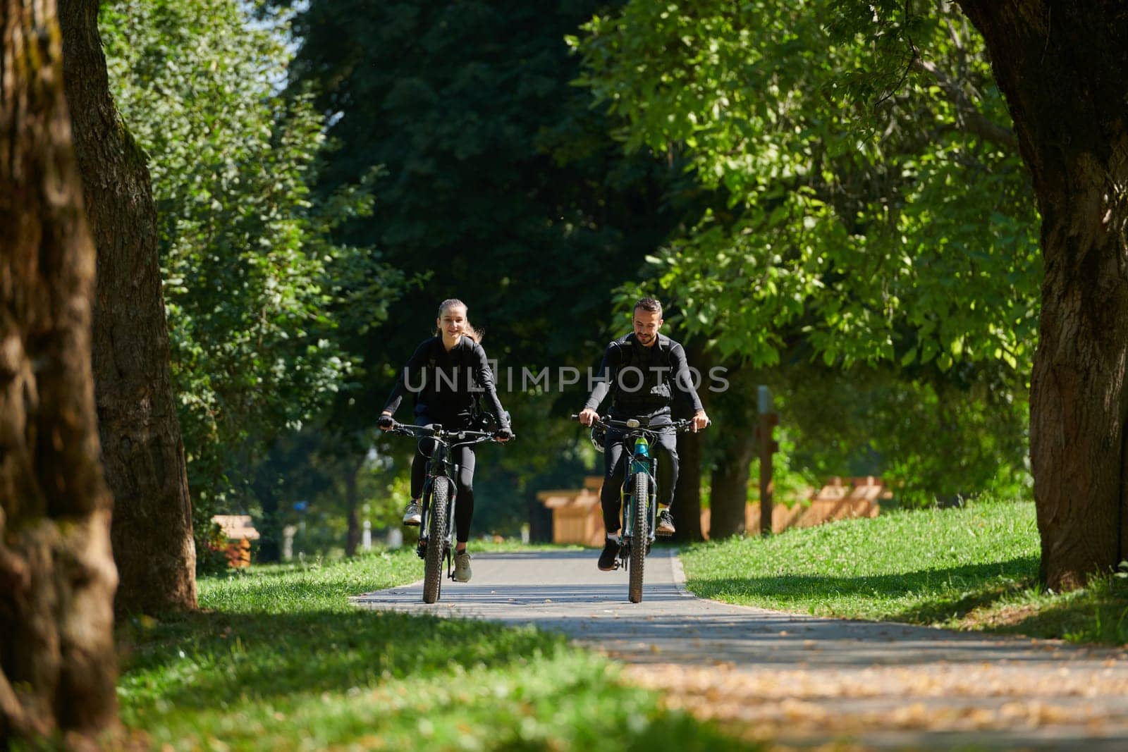 A blissful couple, adorned in professional cycling gear, enjoys a romantic bicycle ride through a park, surrounded by modern natural attractions, radiating love and happiness.