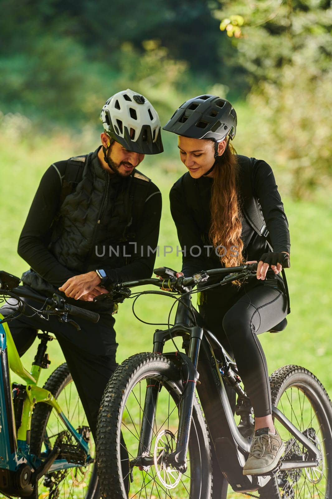 A sweet couple, equipped with bicycles and engrossed in coordinating their journey, checks their GPS mobile and watches while planning scenic routes in the park, seamlessly blending technology and outdoor adventure for a delightful cycling experience by dotshock