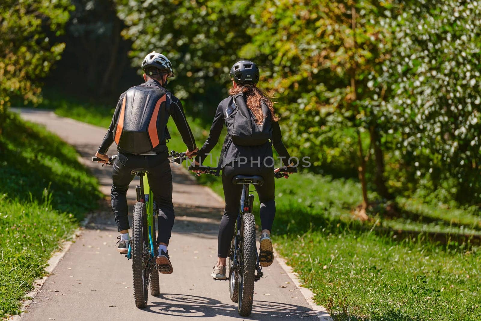 A blissful couple, adorned in professional cycling gear, enjoys a romantic bicycle ride through a park, surrounded by modern natural attractions, radiating love and happiness.